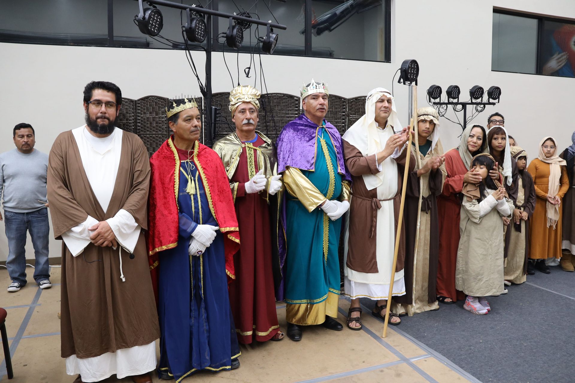 People in colorful historical costumes standing in a row on a stage-like indoor set