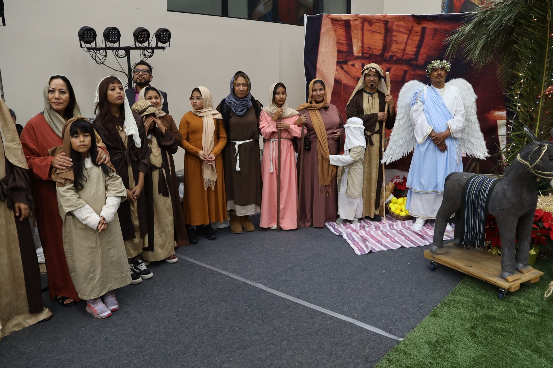 People in costume posing in a nativity scene display outdoors with a manger and sheep figures