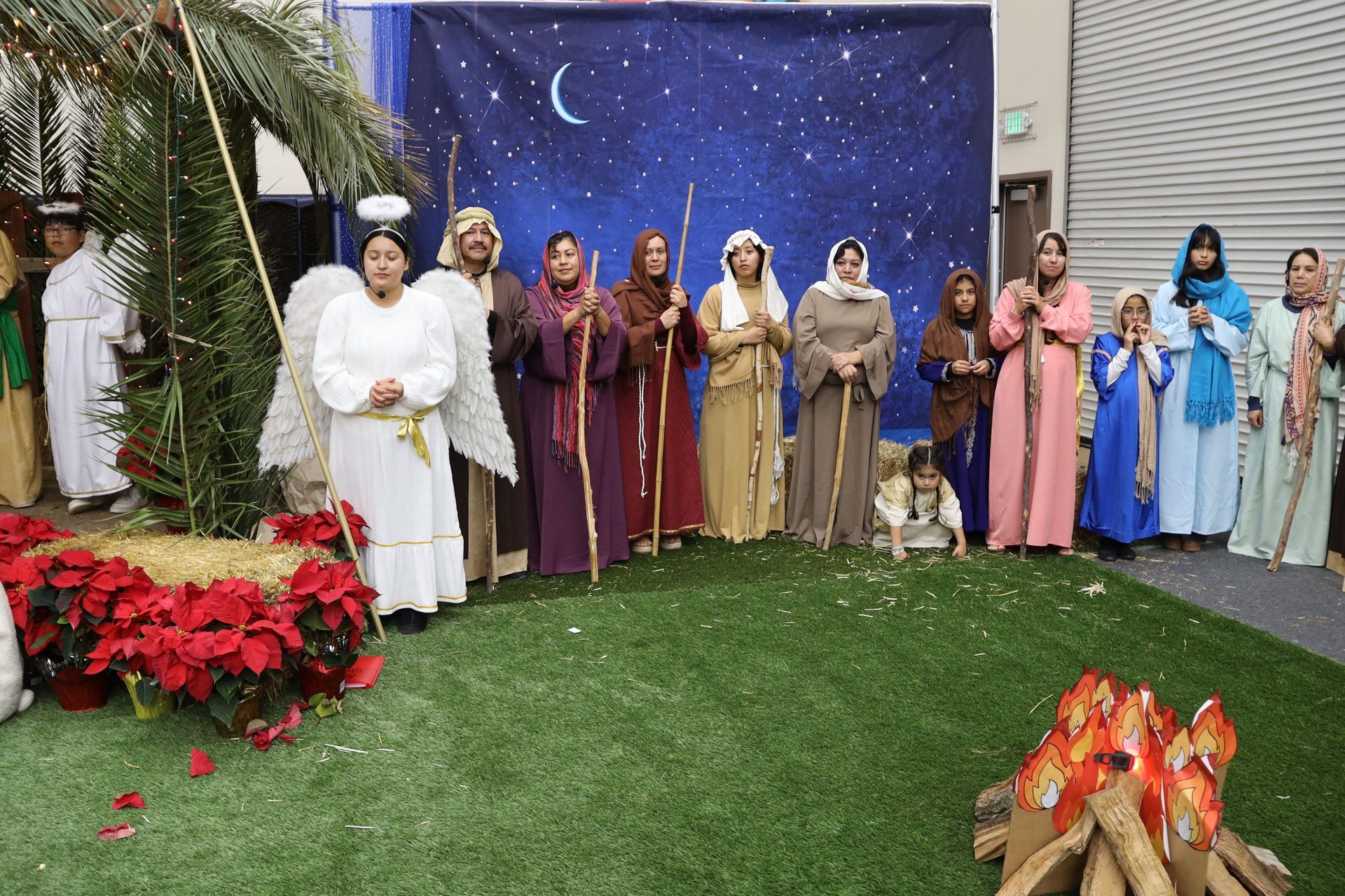 Group of people in colorful robes on a decorated outdoor stage with a starry night backdrop and flowers