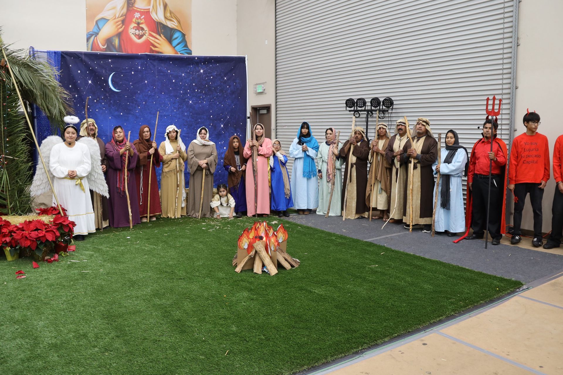 People lined up indoors beside a lit campfire display and a starry backdrop on artificial grass.