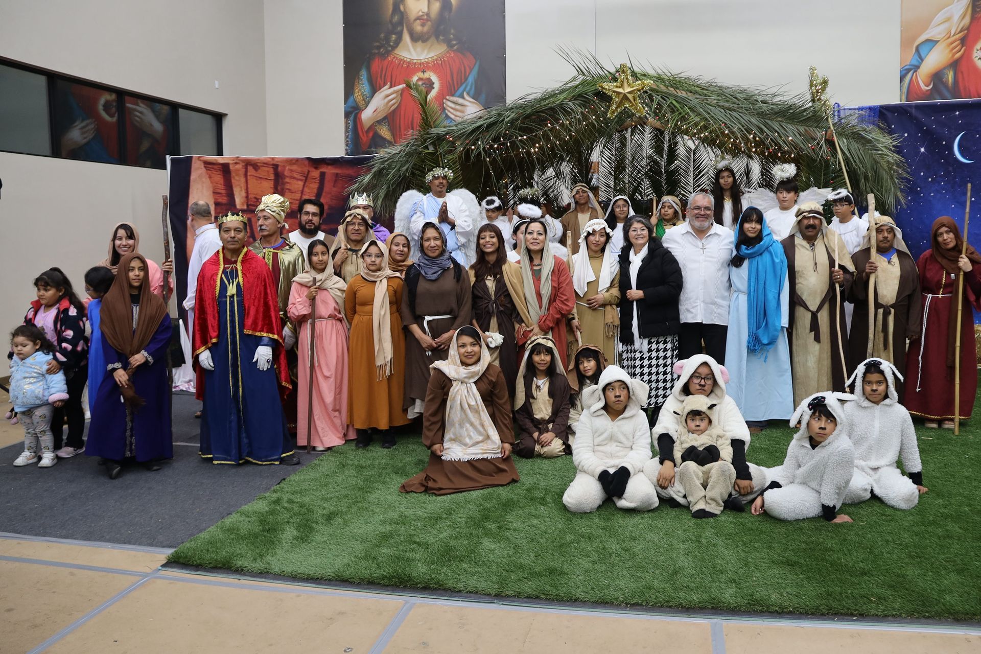 Large group in festive costumes posing indoors under a decorated archway on a stage-like display.