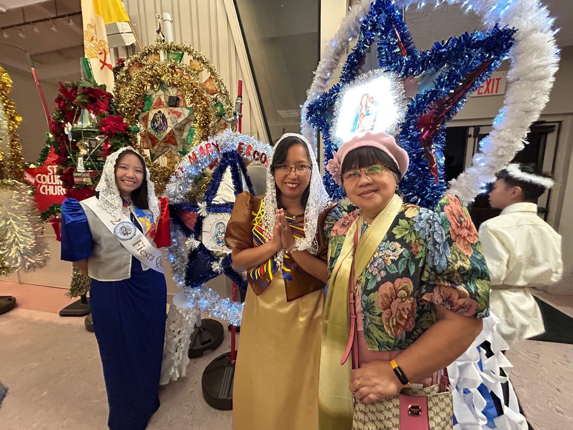 Three people posing with colorful holiday parade floats and wreath decorations indoors