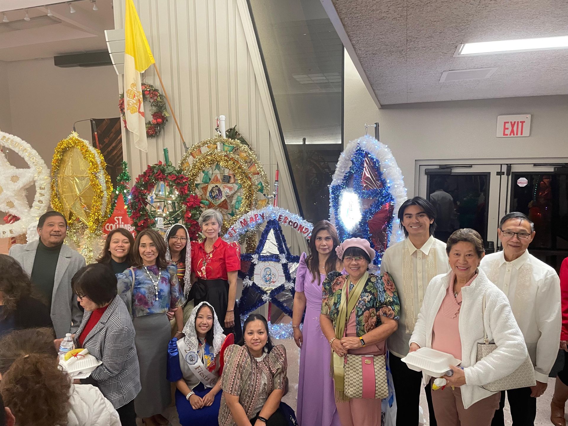 Group posing indoors with colorful decorative frames and an exit sign in the background