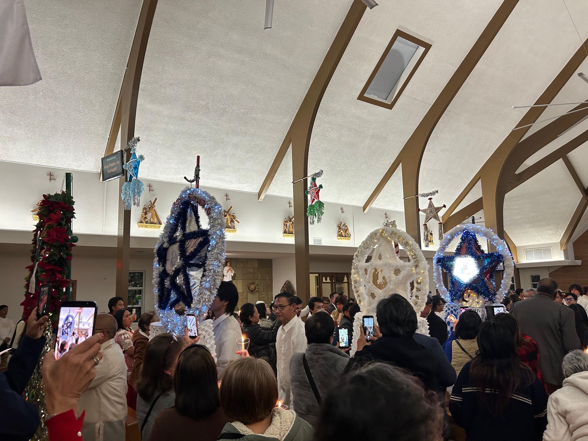 Crowded indoor festival with people watching decorated hanging star lanterns under arched ceiling beams