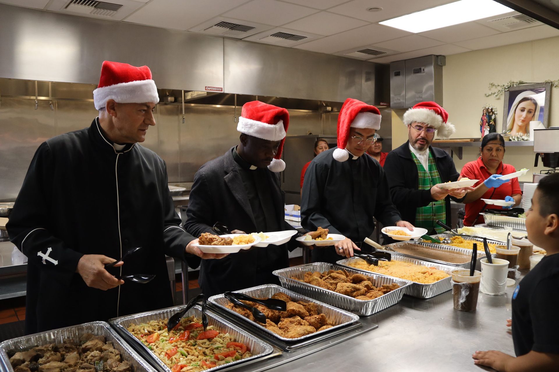 People in Santa hats serving food from a buffet line in a kitchen or cafeteria