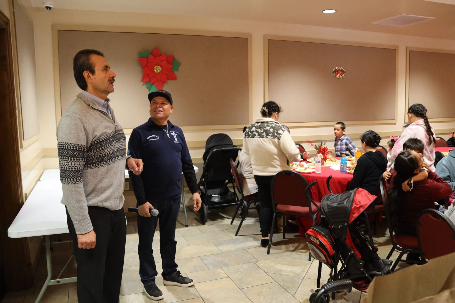 People seated at a festive dining table in a restaurant, with two men standing nearby.