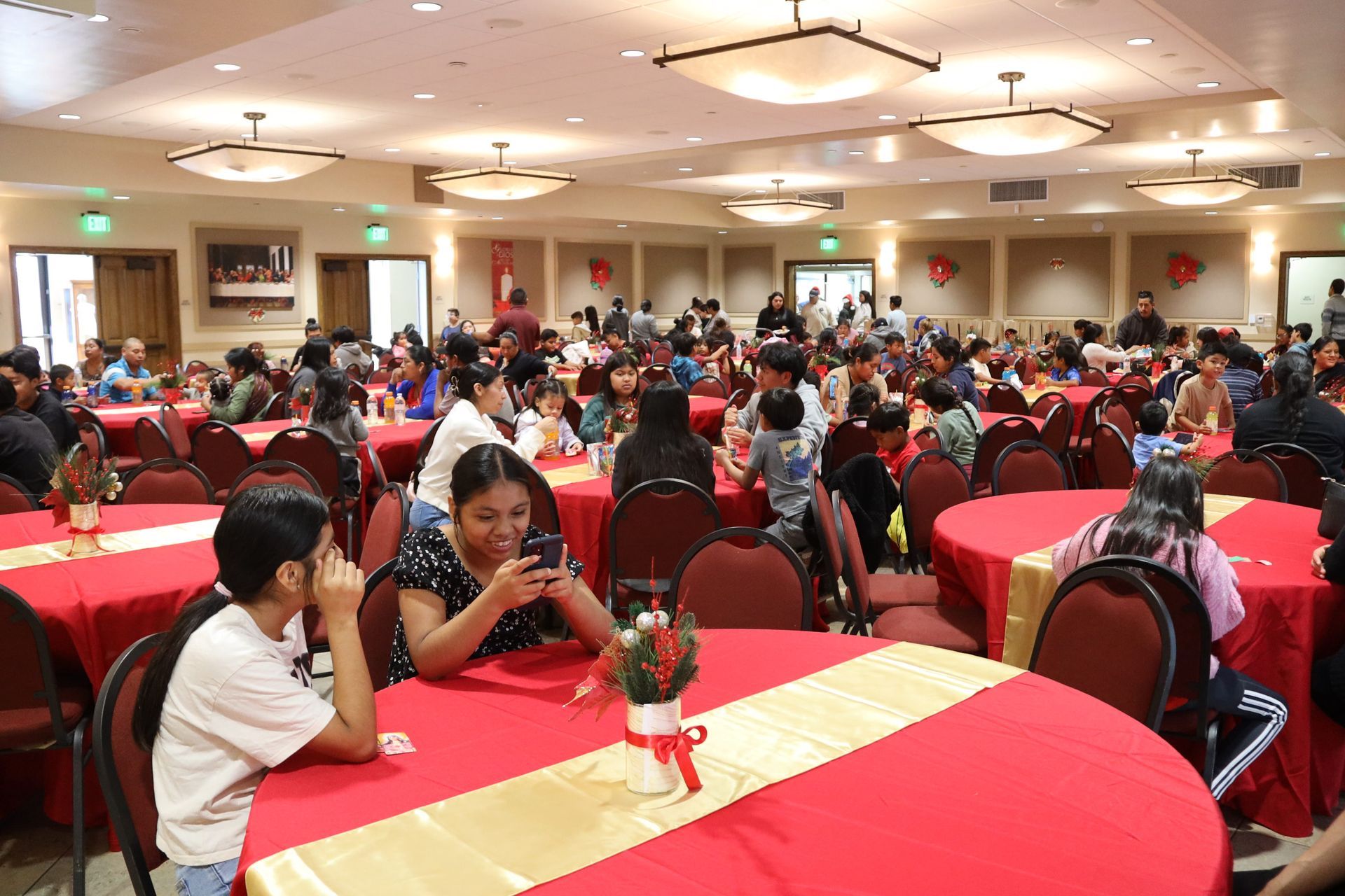 People seated at red-covered tables in a large banquet hall, talking and eating.