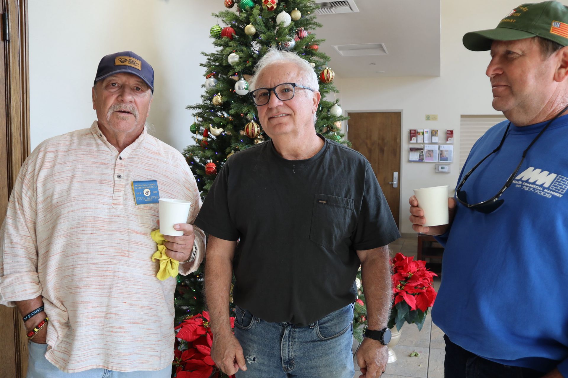 Three people standing indoors in front of a decorated Christmas tree.