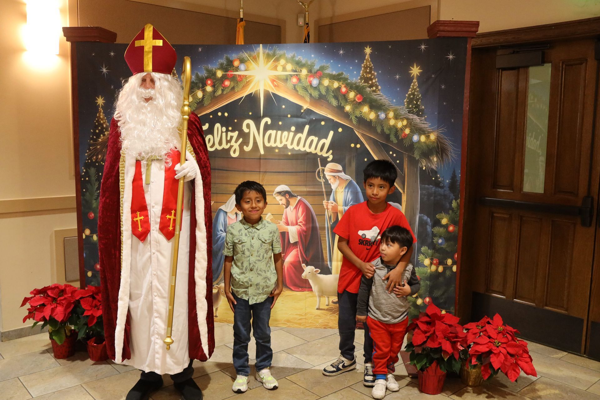 Santa posing with three children in front of a Christmas backdrop and poinsettias