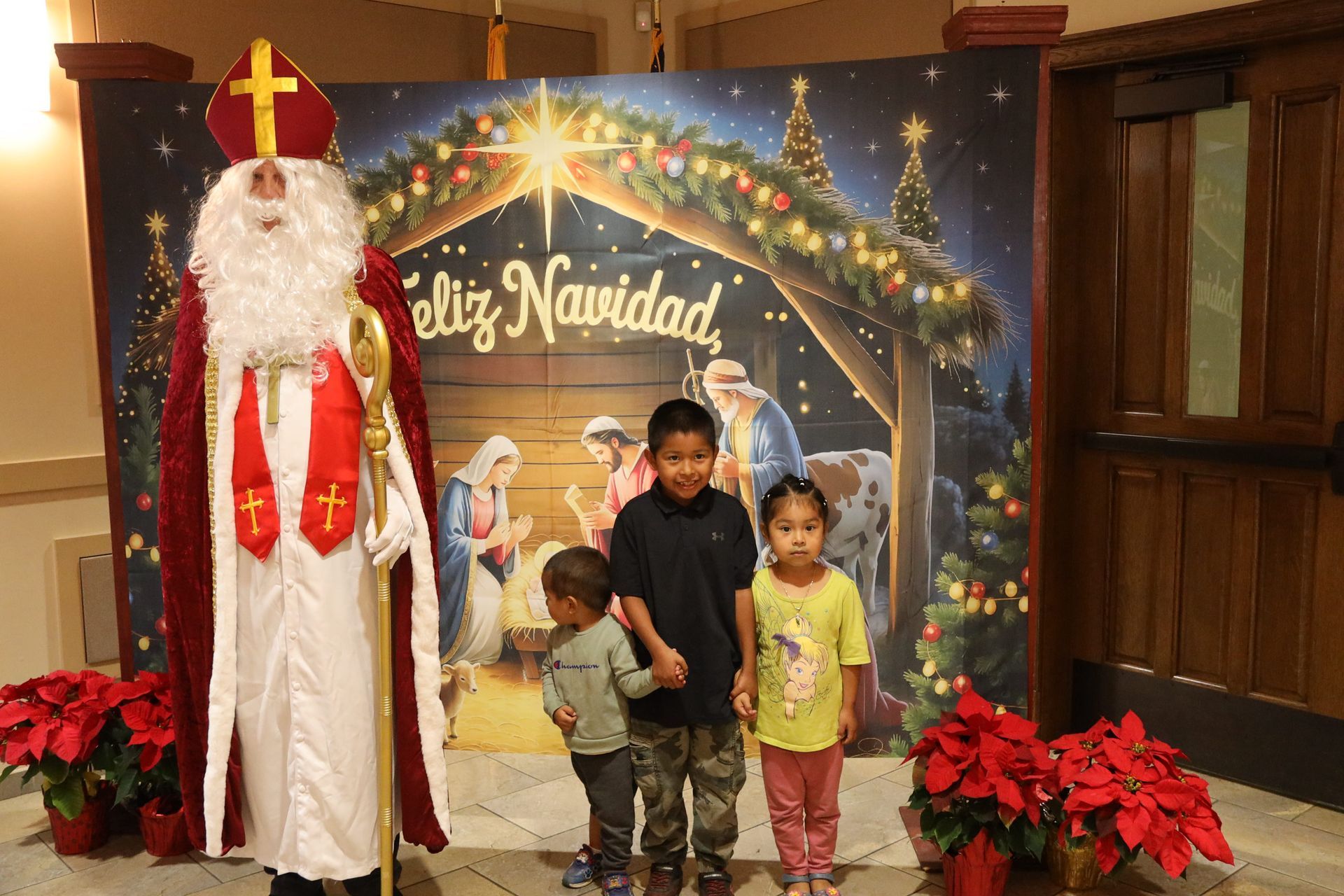 Family posing with Santa Claus in front of a Christmas “Feliz Navidad” backdrop and poinsettias