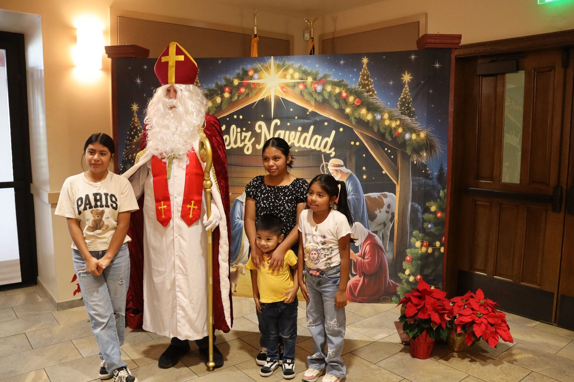 Santa posing with three children beside a festive holiday backdrop and red poinsettias