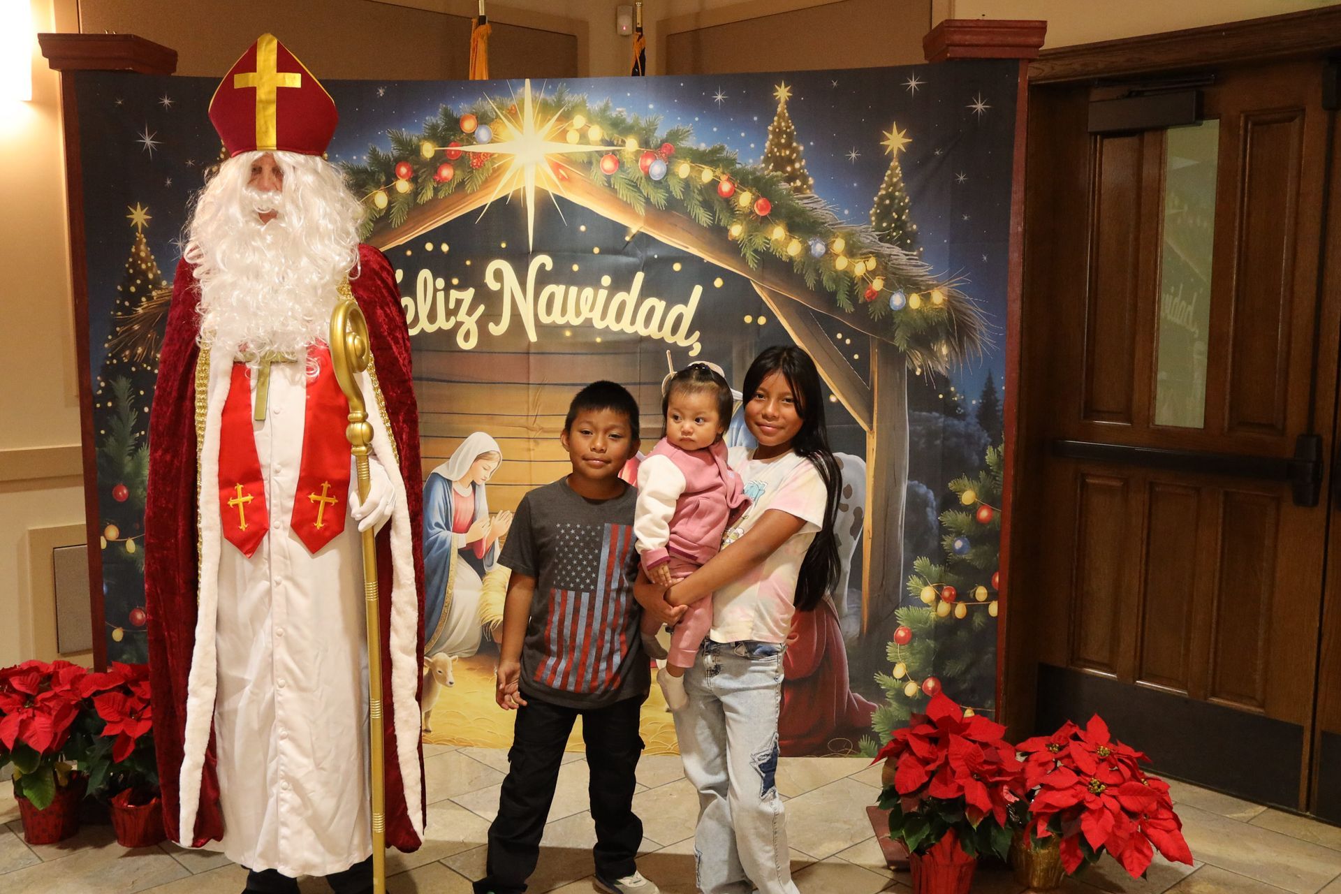 Santa posing with three children in front of a festive “Feliz Navidad” holiday display.