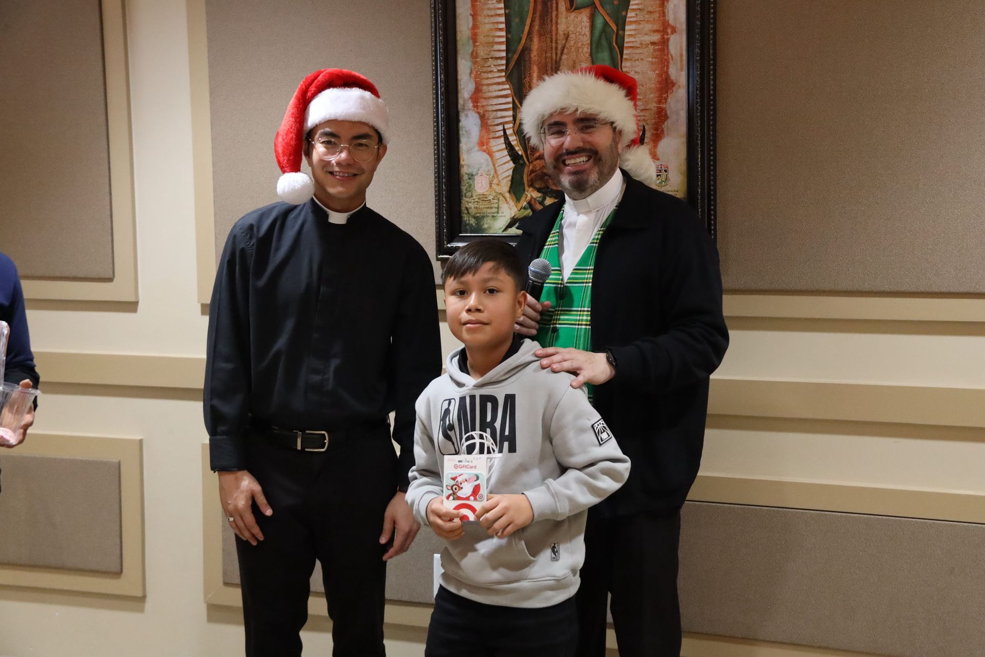 Three people posing indoors, two in Santa hats with a boy holding a gift box.