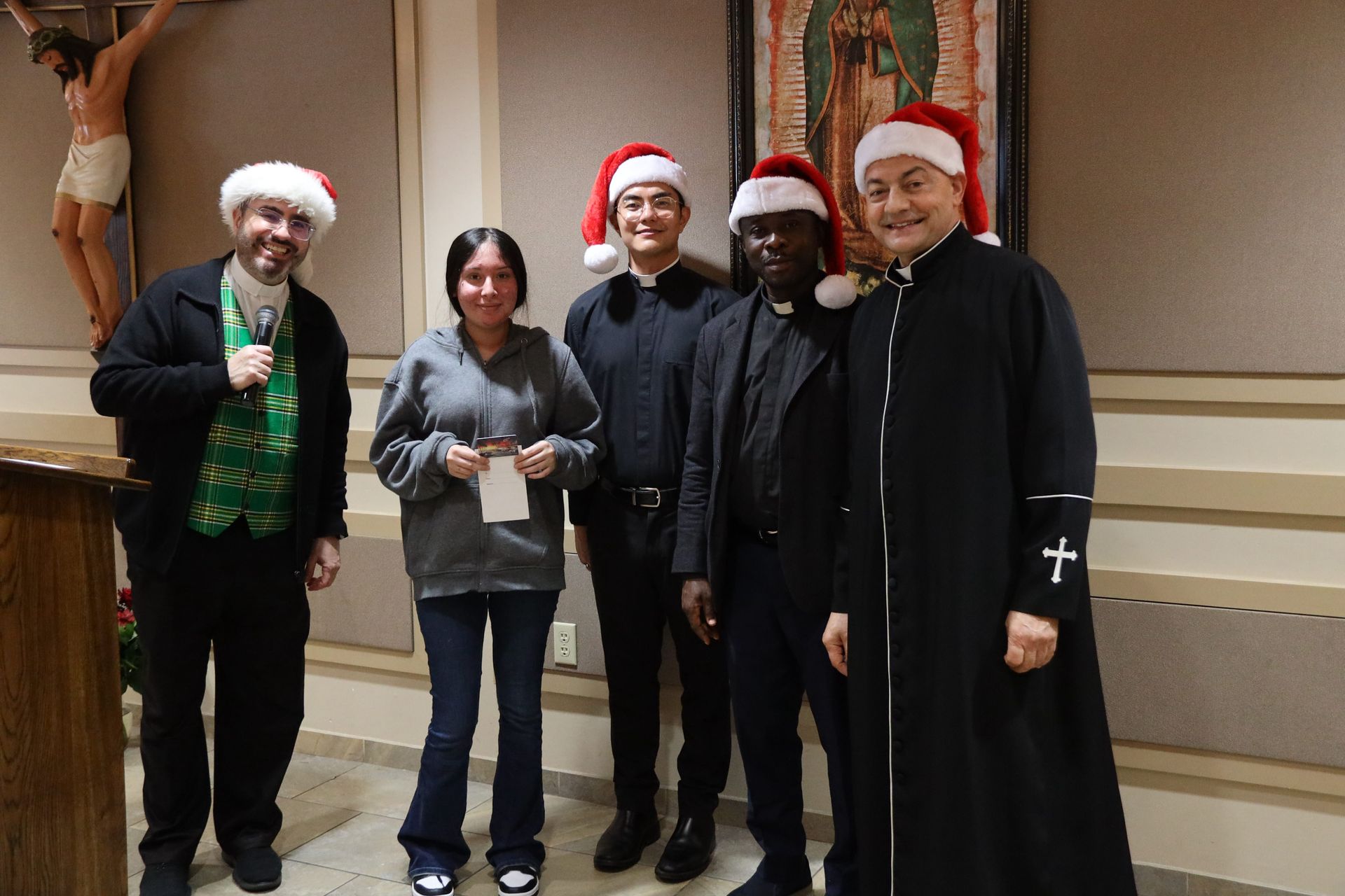 Five people in Santa hats posing indoors, one holding a green drink, with a small statue in the background