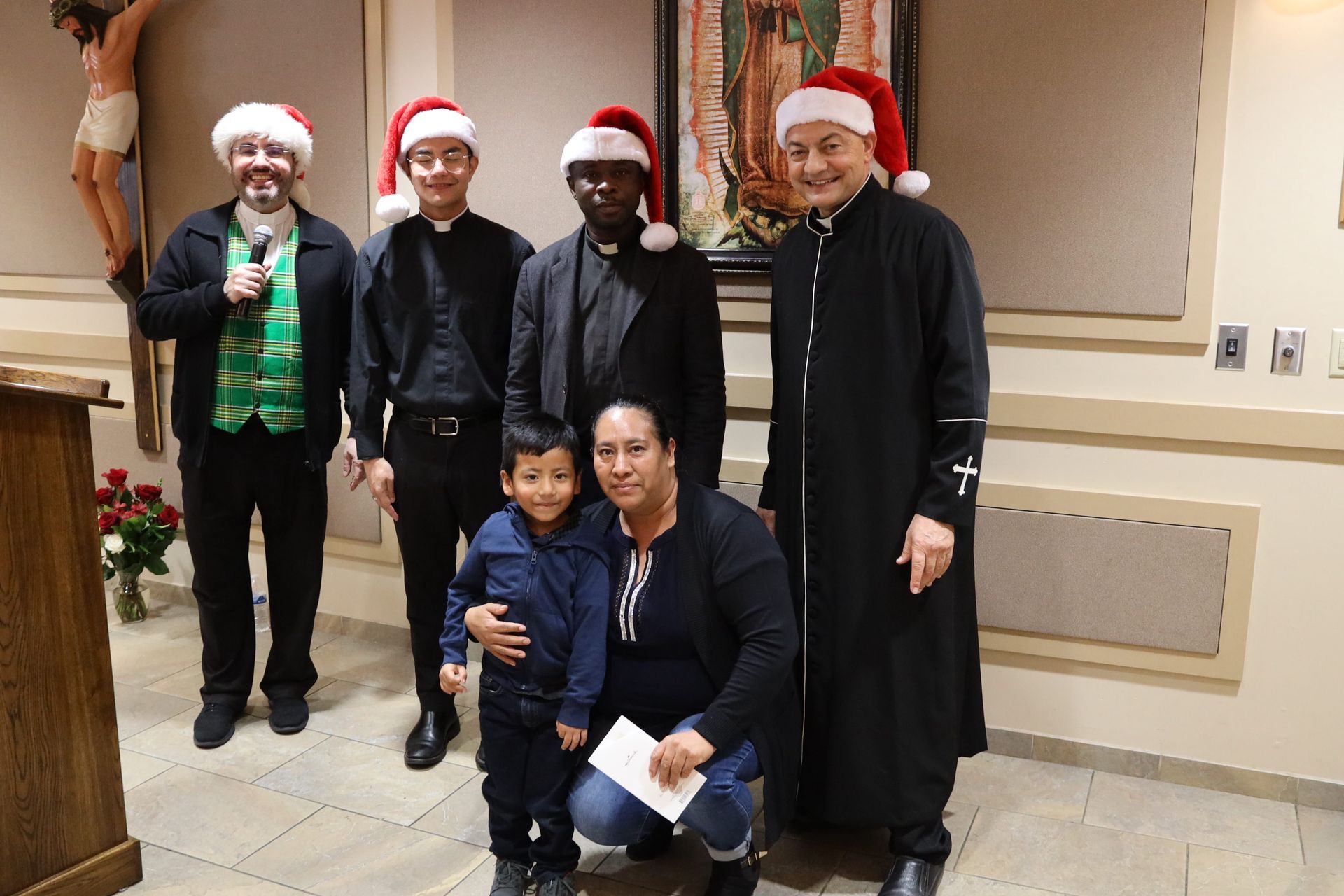 Group posing indoors, several wearing Santa hats, with two people kneeling in front.