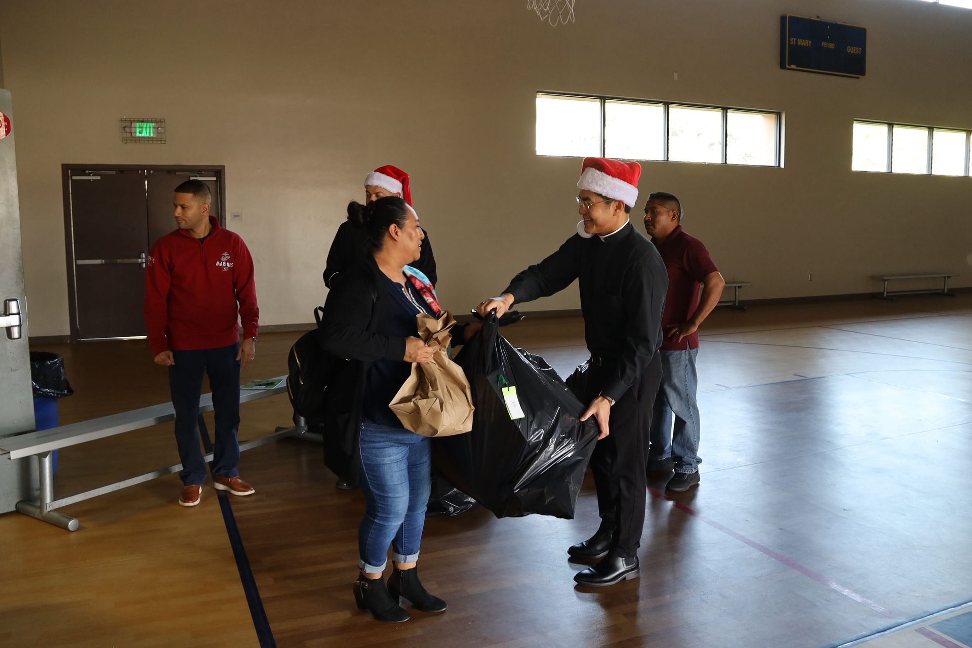 People in Santa hats hand a large black bag in an empty gymnasium.
