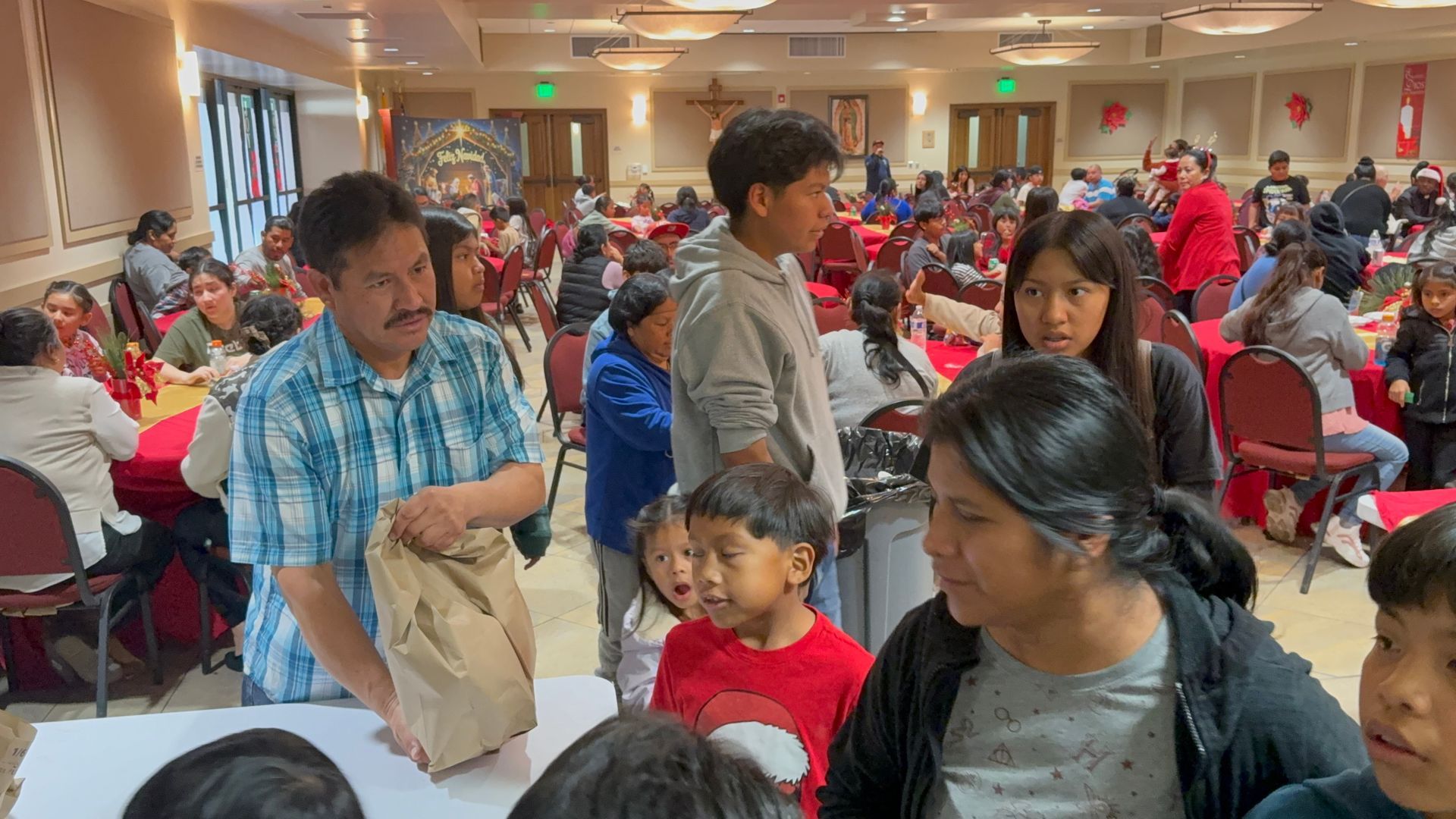 People seated in a crowded banquet hall, with several standing near a table in the foreground.