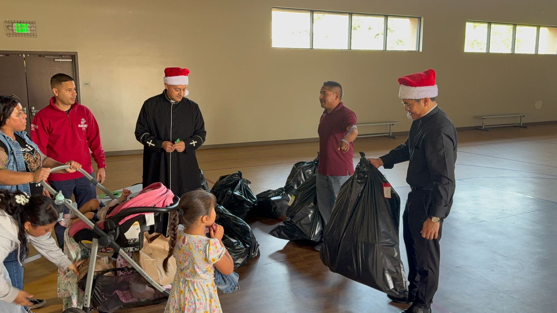 Volunteers in Santa hats sort bags of donated clothes in a community hall.