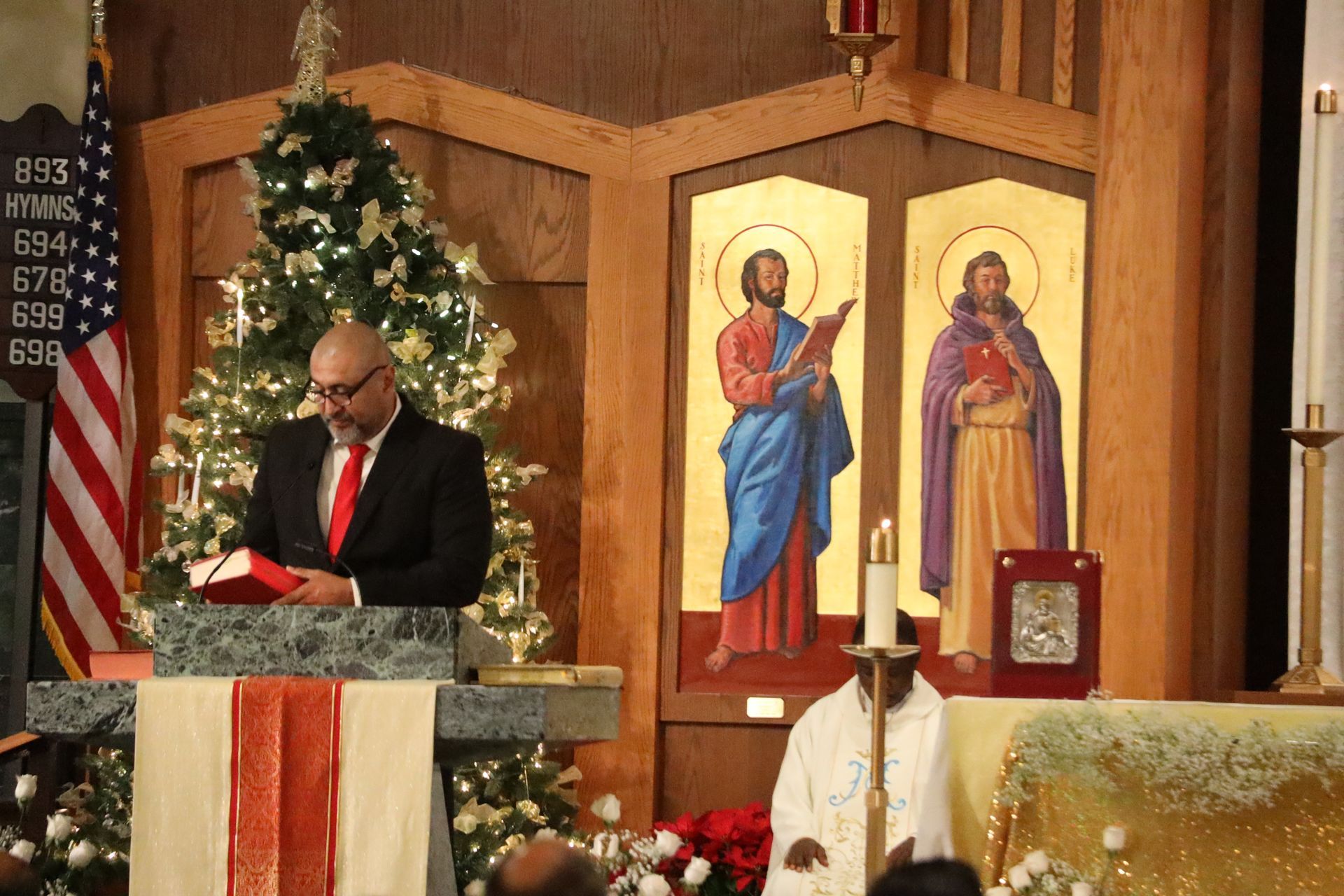 Man in suit reading at church altar beside Christmas tree and religious icons