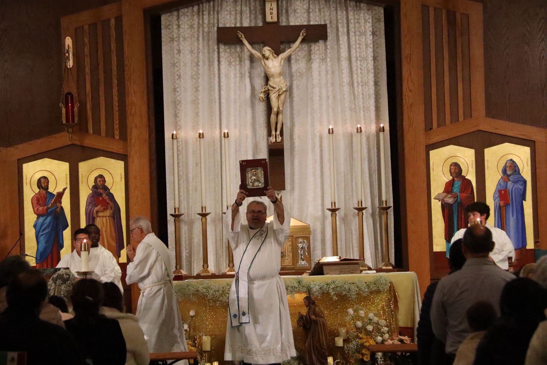 Priest at altar during church service, with crucifix, icons, and congregants standing nearby