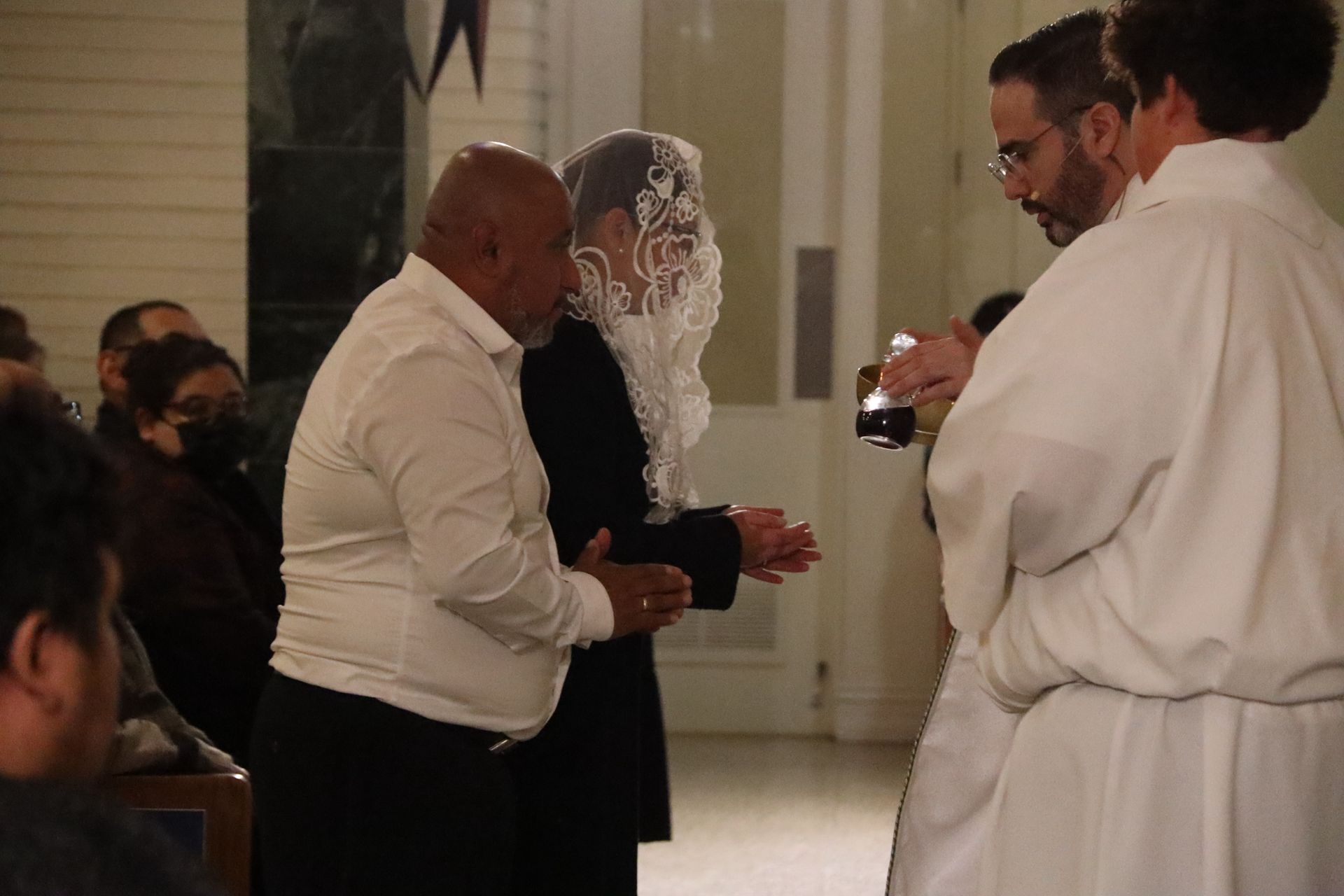 Two people holding hands during a ceremony while a robed officiant stands nearby and films them.