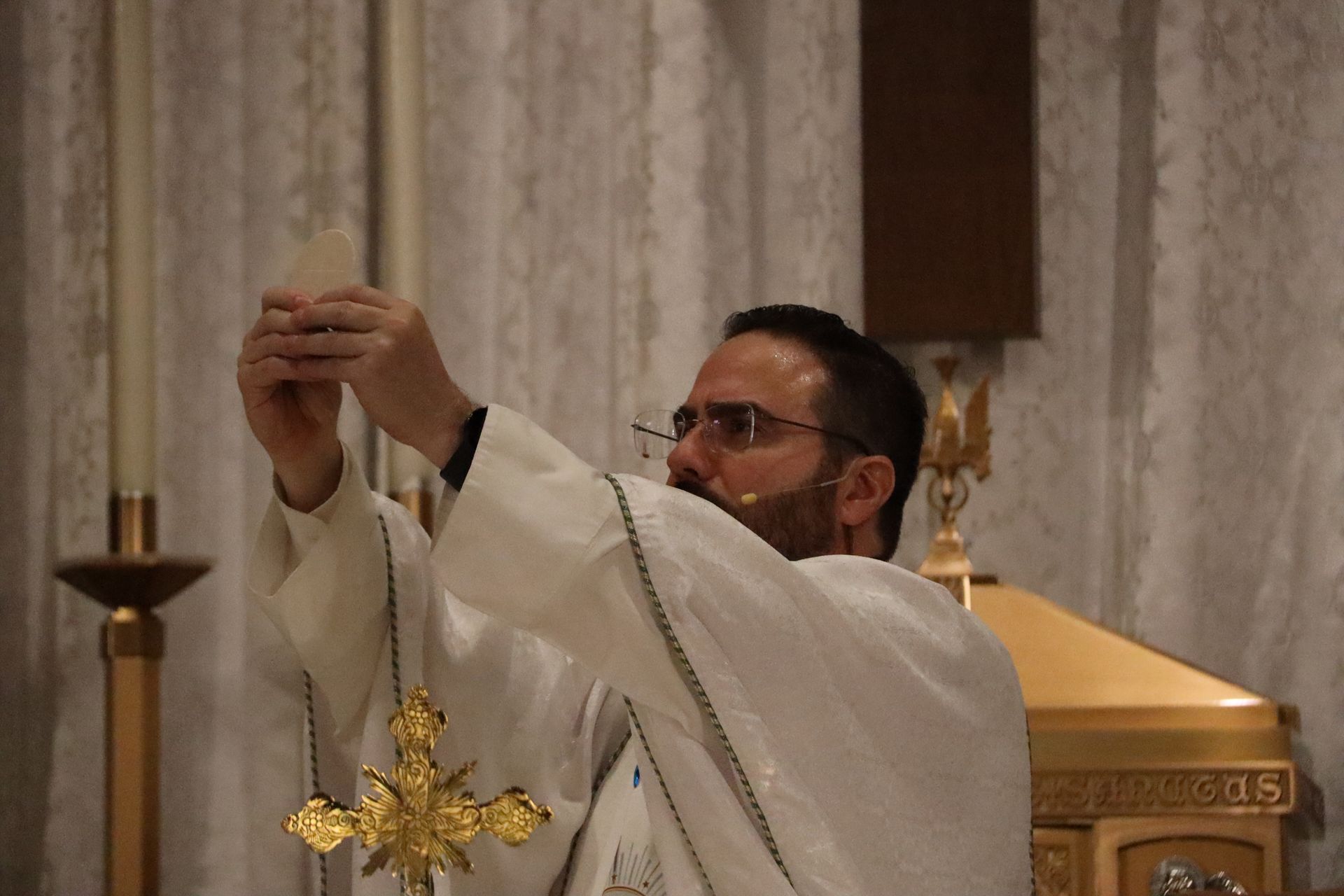Priest in white robes elevates a gold cross during a church service