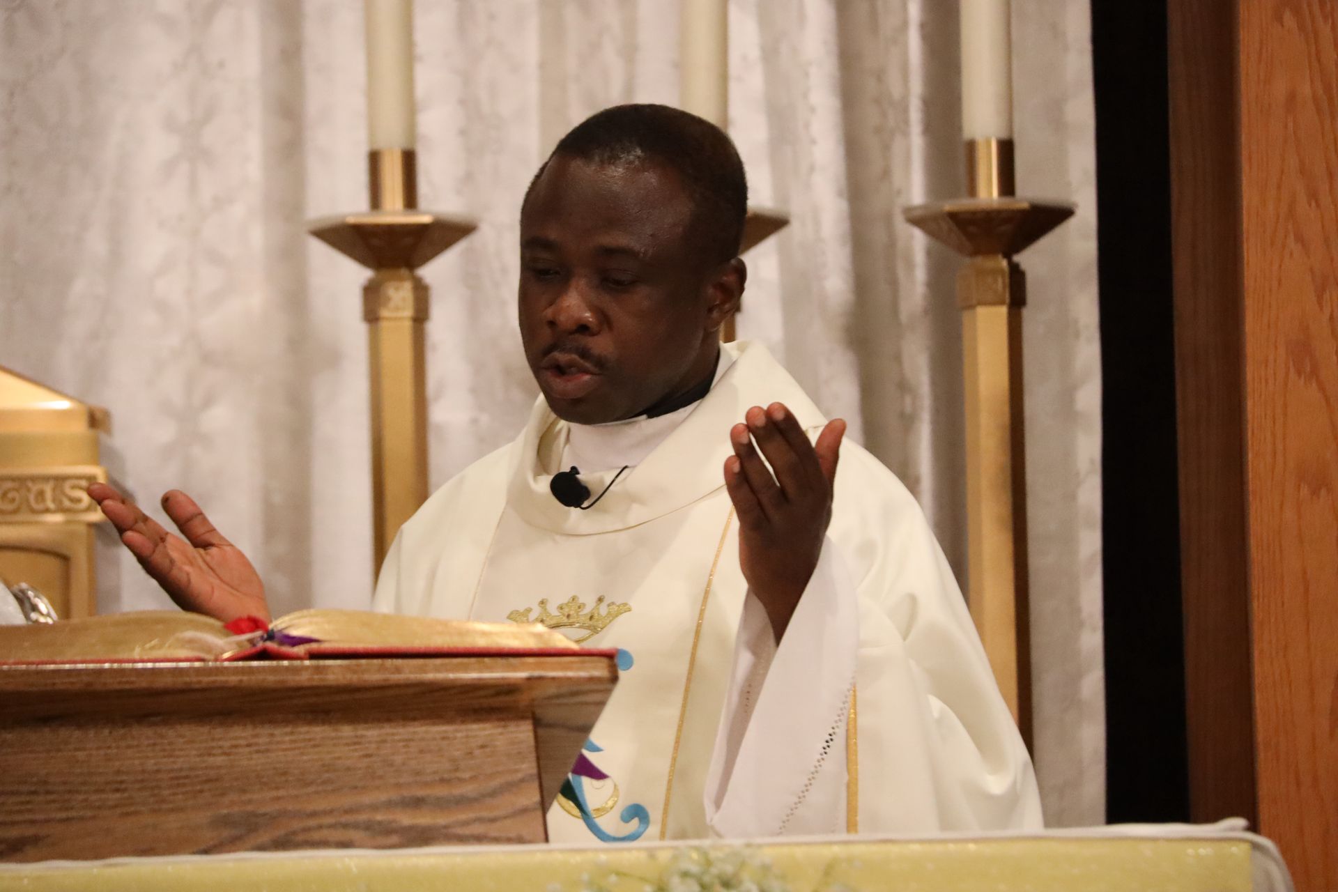 Priest in white vestments speaking at a church altar with hands raised