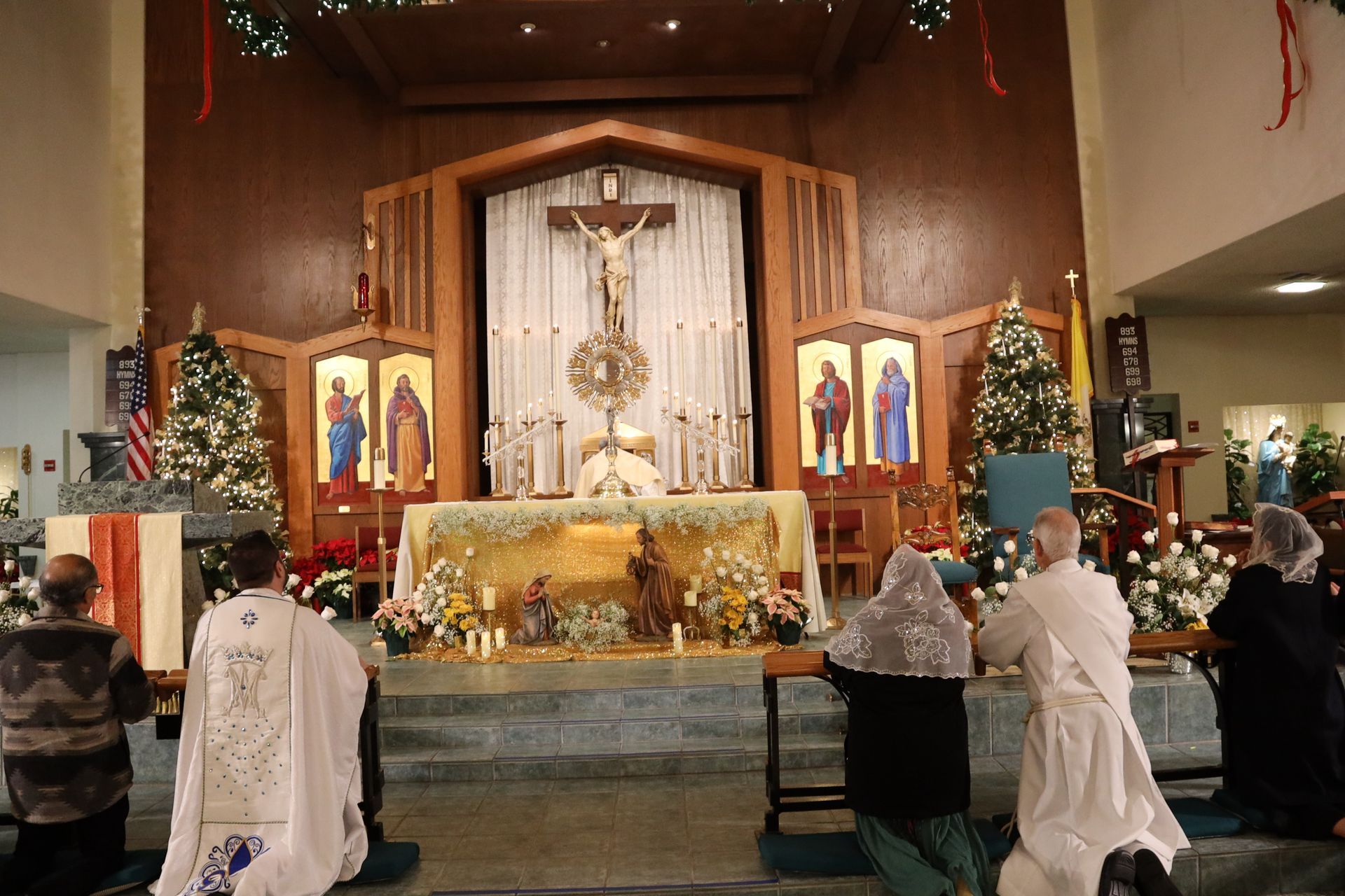 Church altar with crucifix and candles, people kneeling in prayer during a religious service