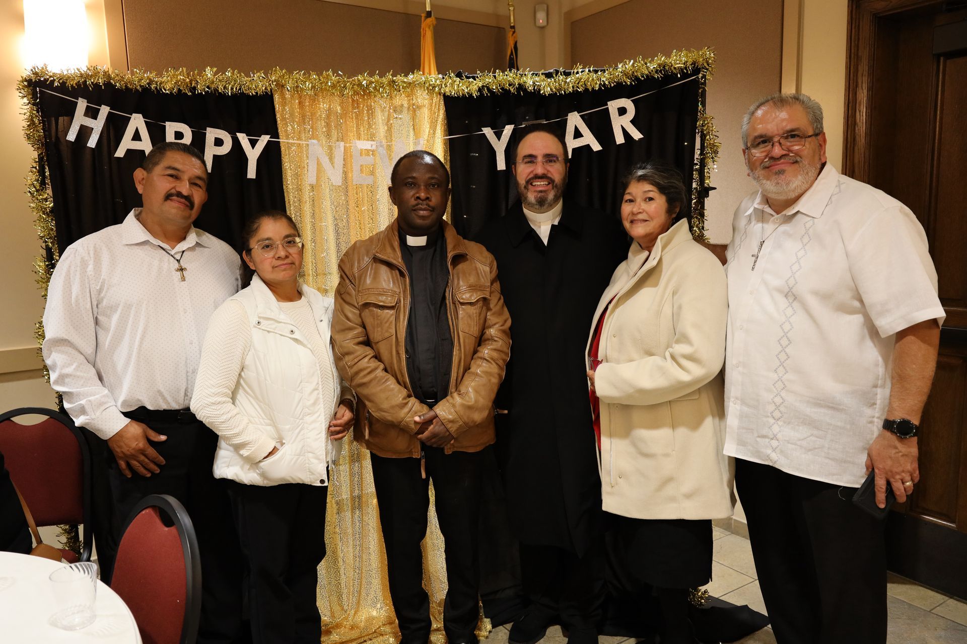 Six people posing indoors in front of a “Happy New Year” banner, dressed in business attire.