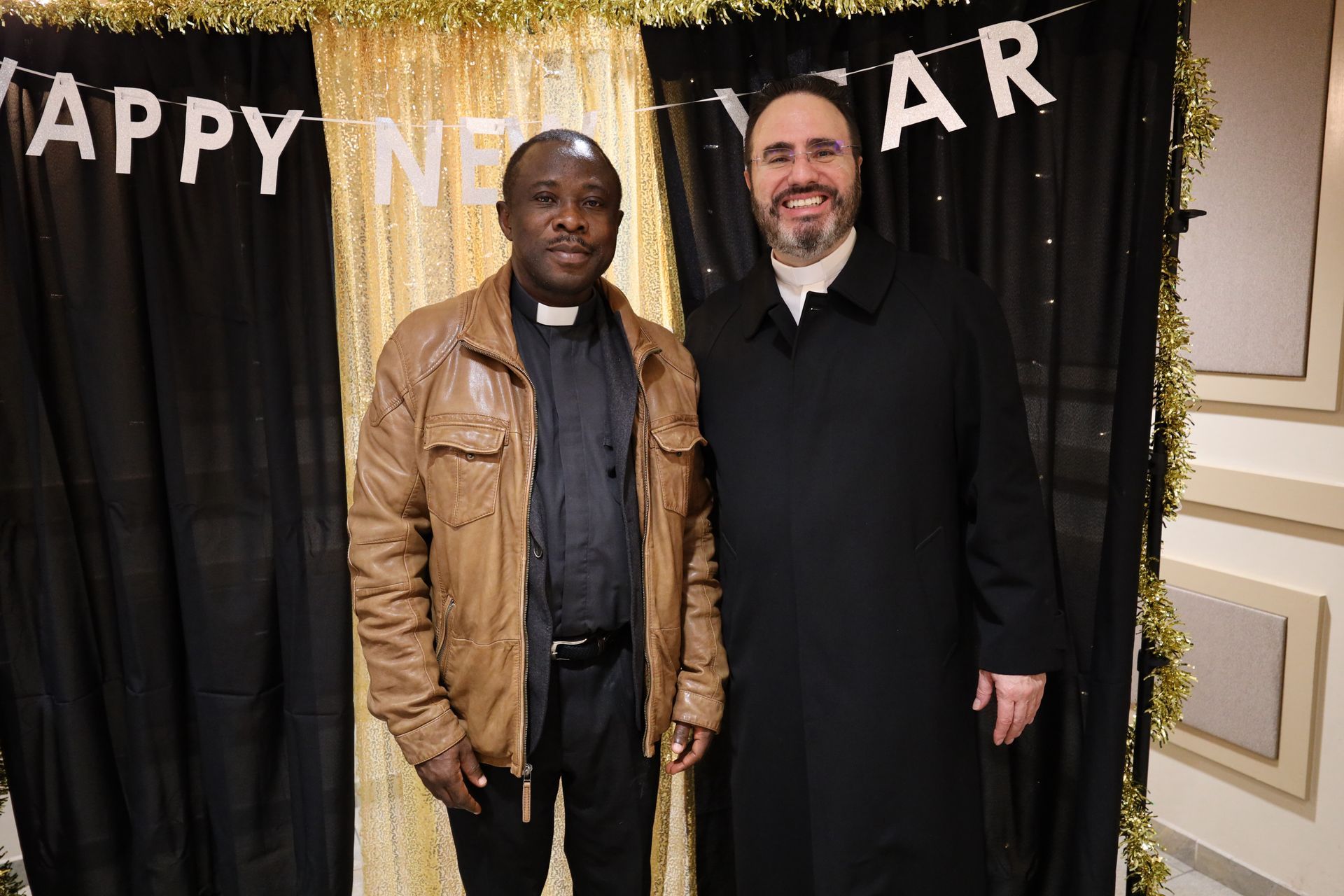 Two men posing in front of a New Year banner and black curtain backdrop