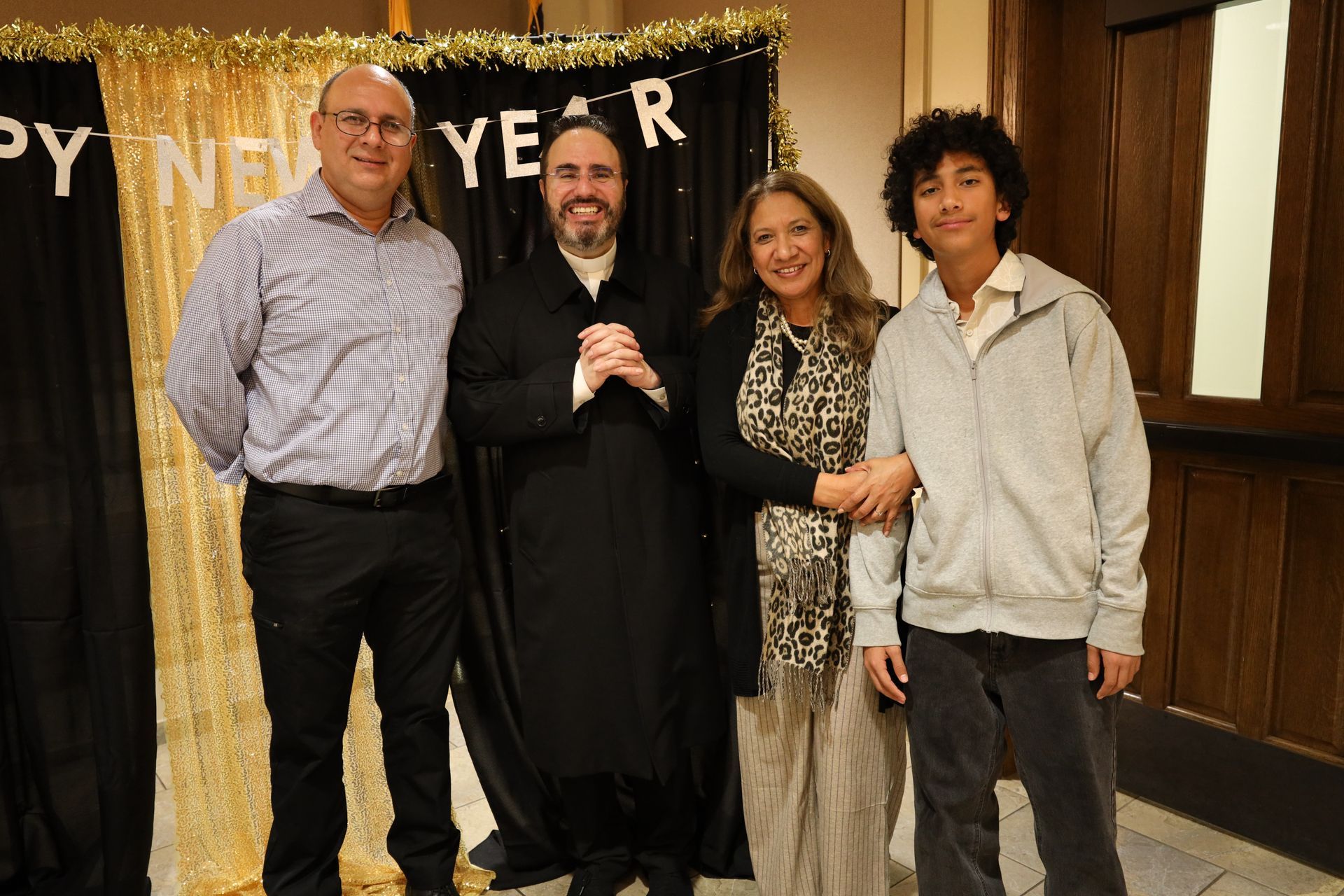 Four people posing at a formal event in front of a banner, smiling and dressed casually and semi-formally