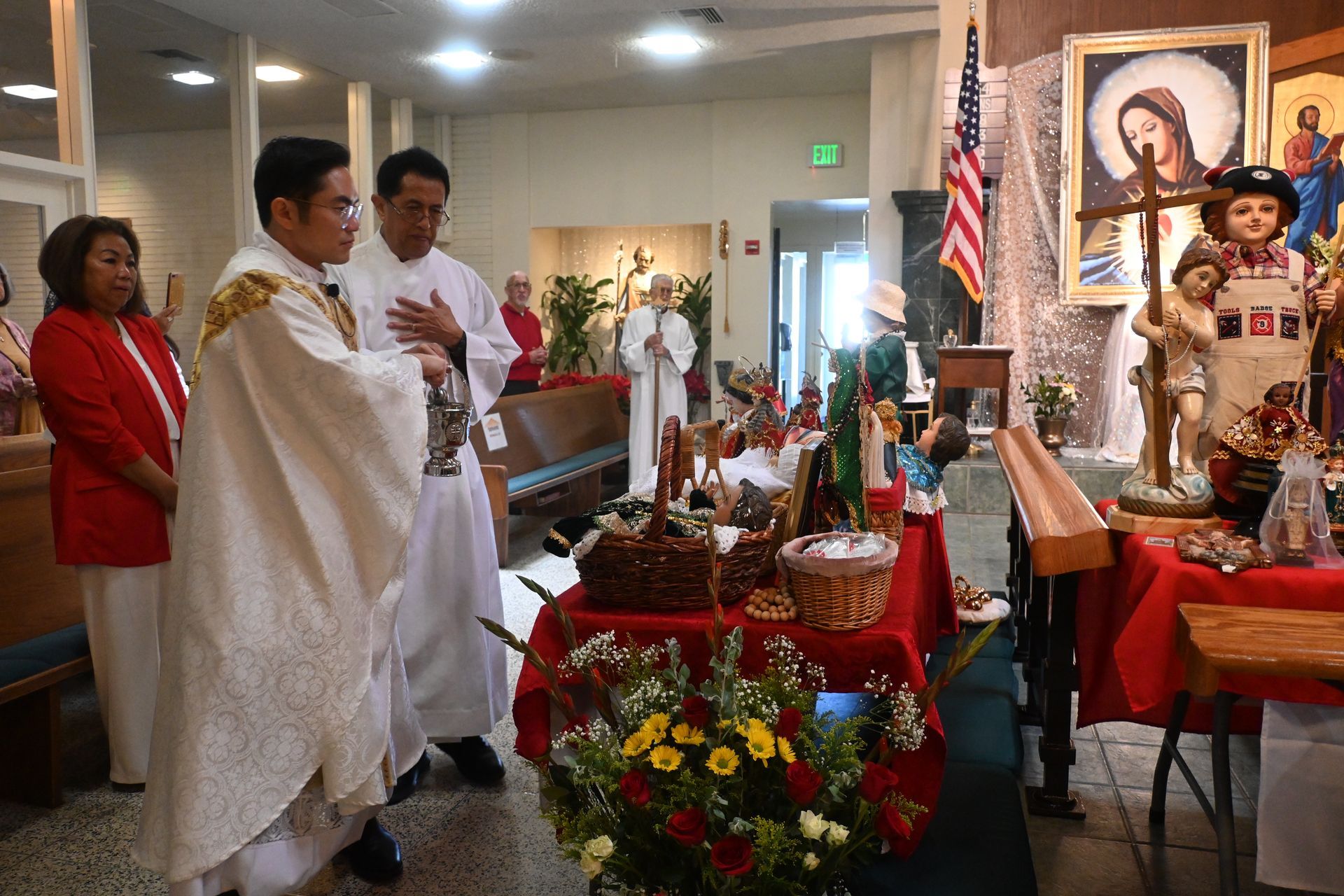 People in white robes attend a religious ceremony beside an altar with flowers and candles.