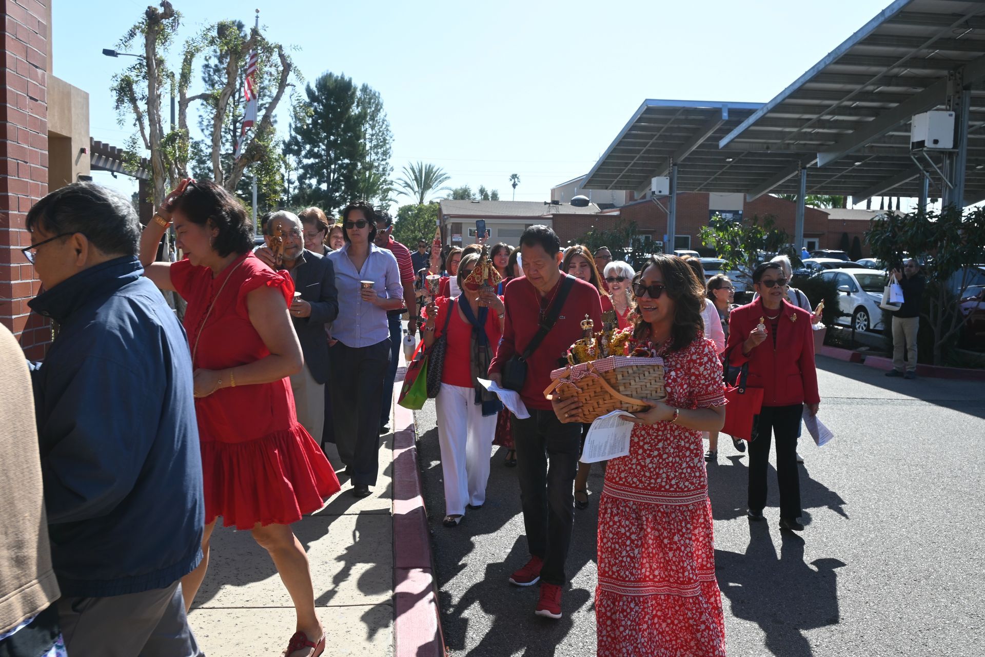 People in red outfits walking outdoors at a lively public event under a canopy