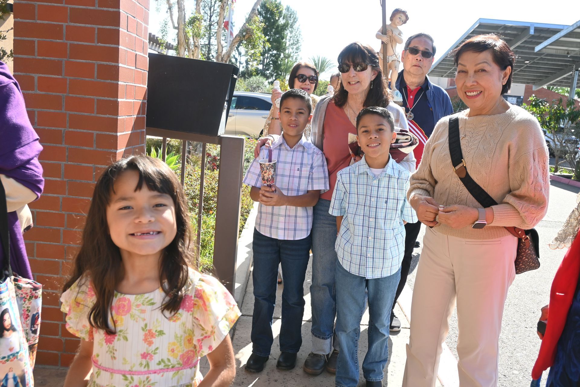 Group of children and an adult standing outdoors in bright sunlight, smiling at the camera.