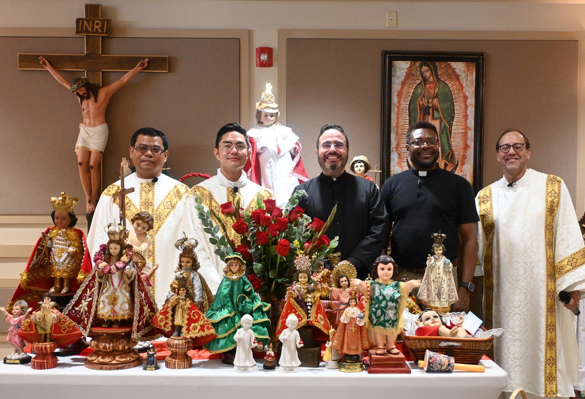Six people posing behind a decorated altar with statues, flowers, and a crucifix in a church.