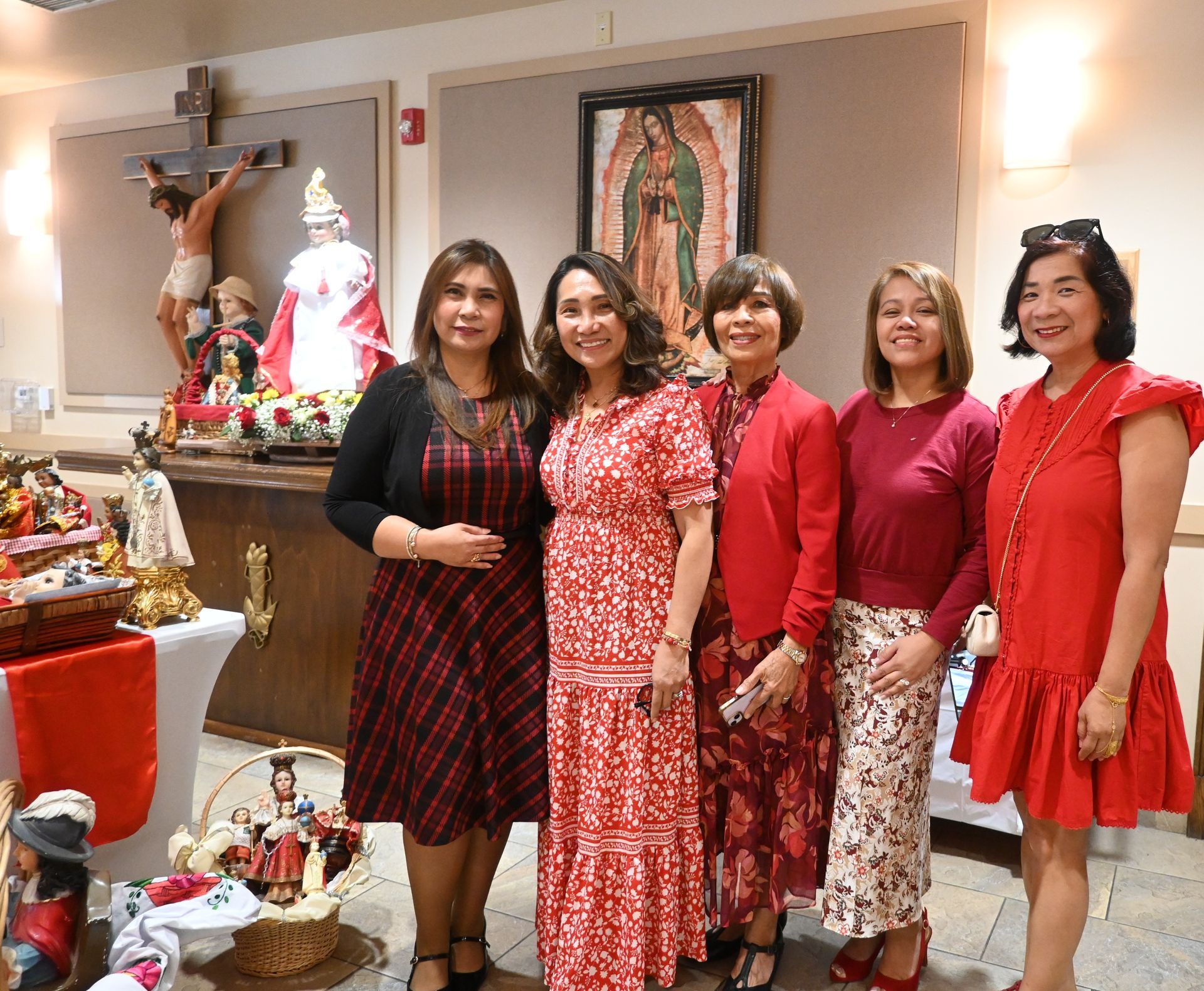 Five women pose indoors beside a religious shrine and nativity display.