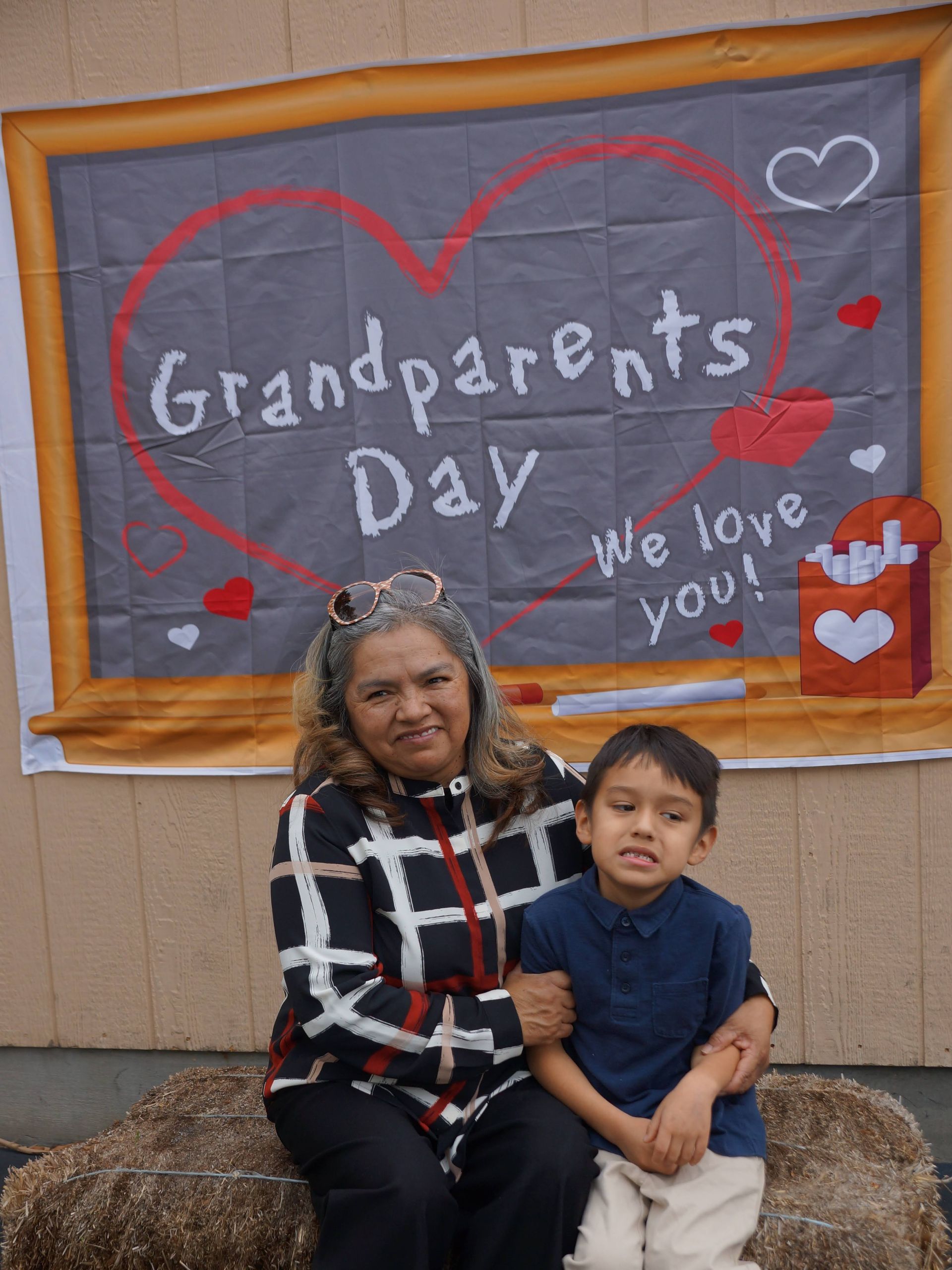 Woman and child seated in front of a “Grandparents Day” chalkboard display with hearts and “We love you!” signs