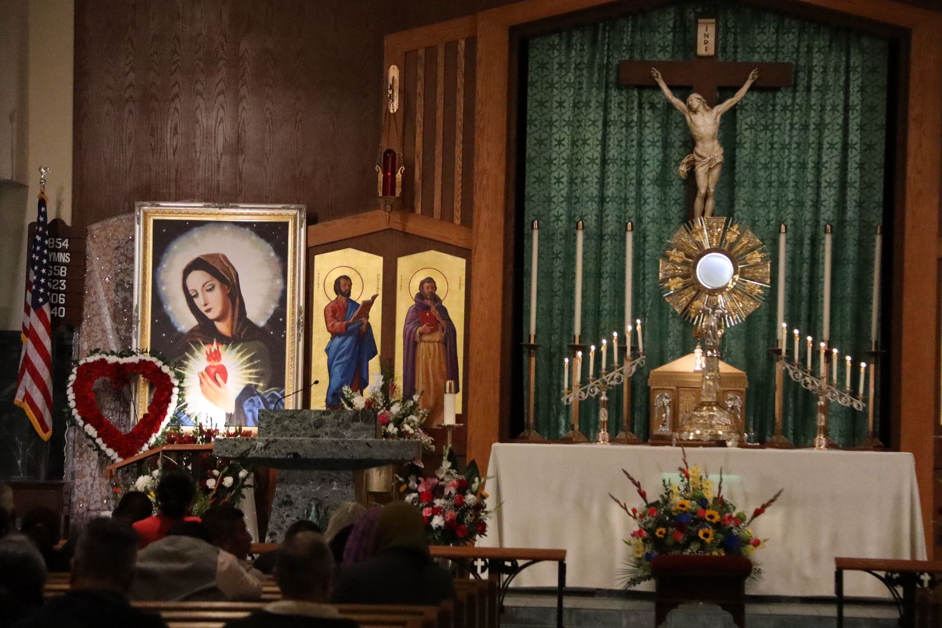 Catholic altar with crucifix, candles, framed icons, and floral arrangements in a chapel