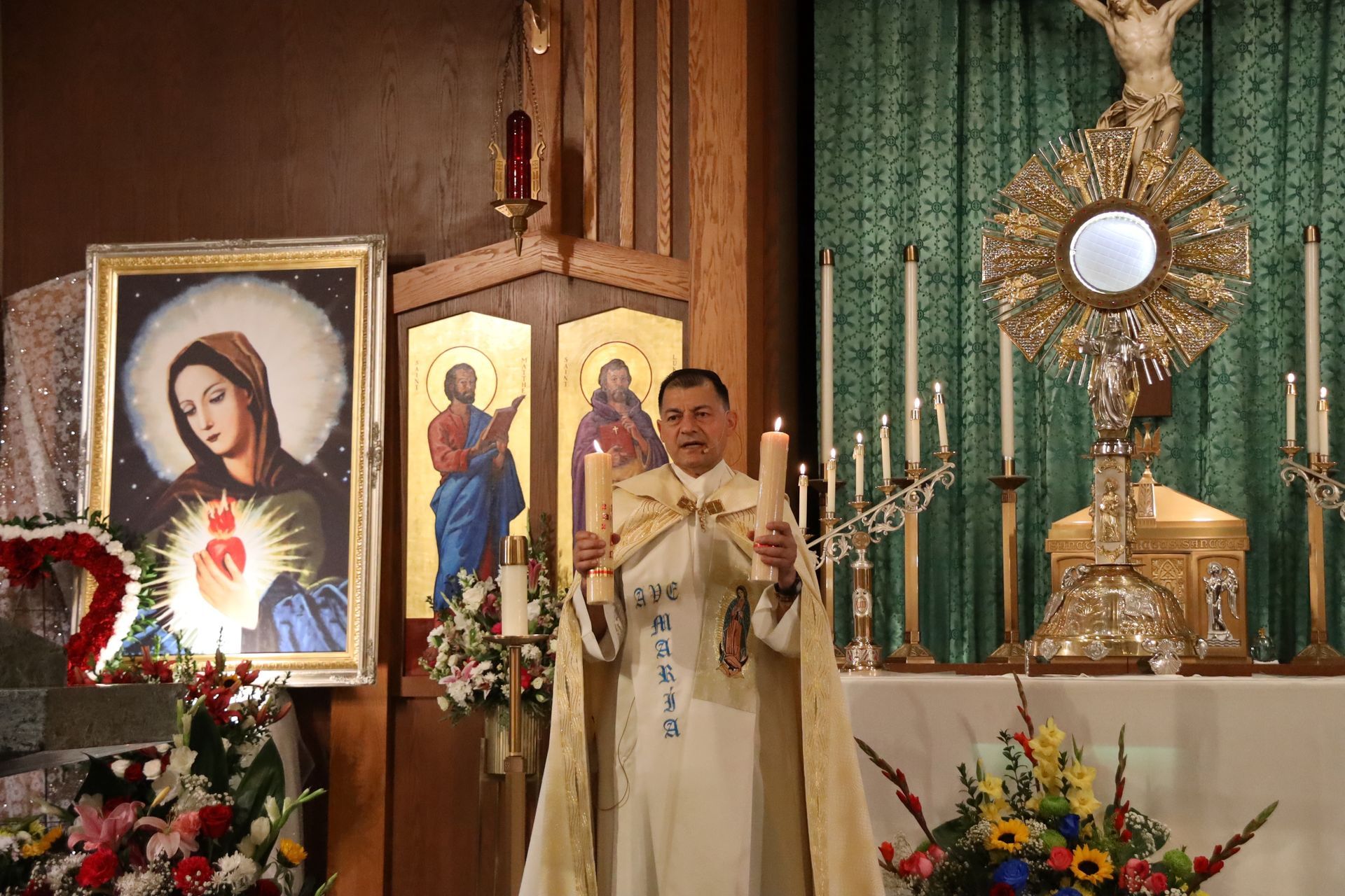 Priest officiating Mass at a church altar with religious icons, candles, and flowers