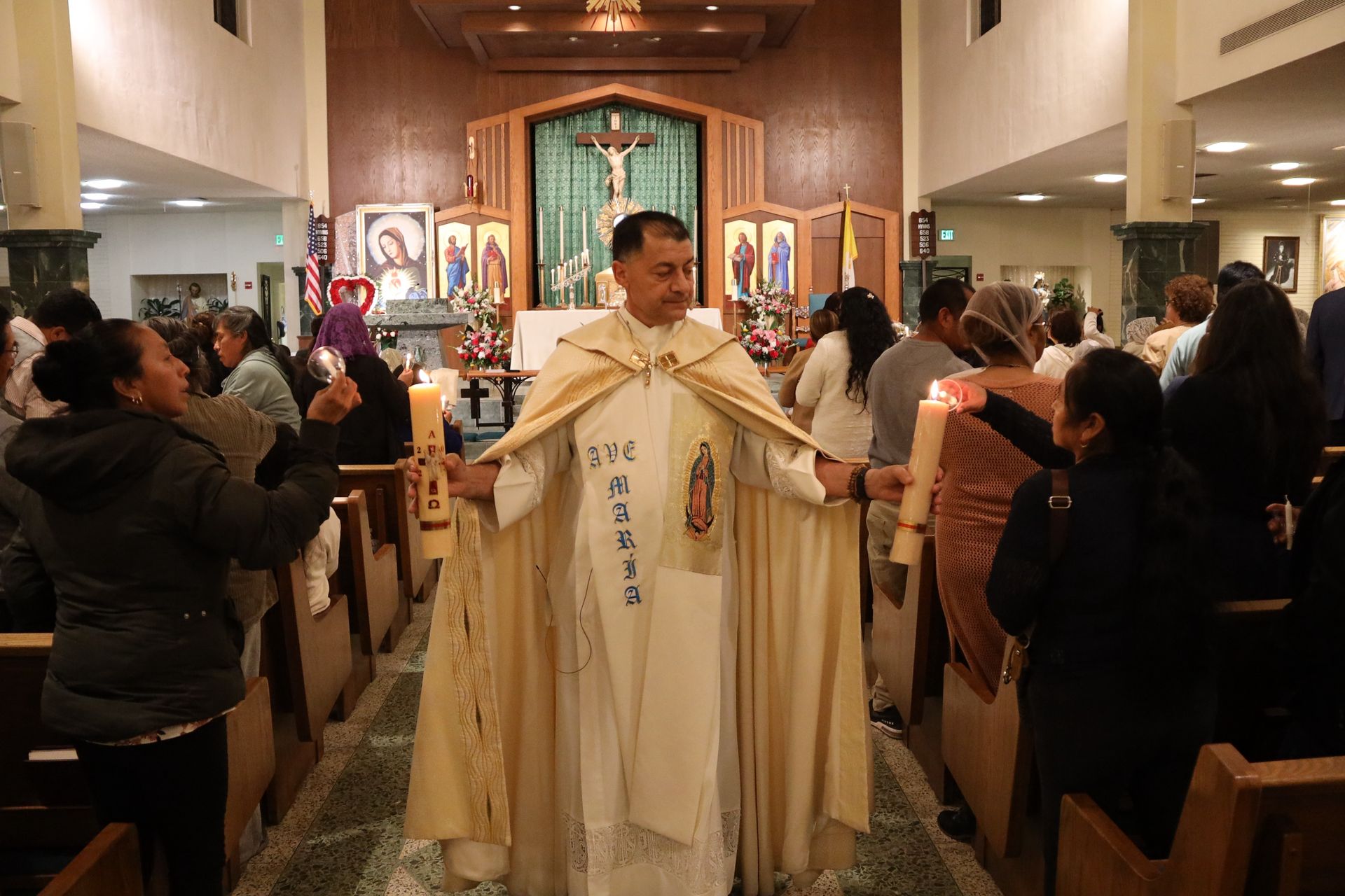 Priest in cream vestments greets a congregation in a church aisle during a service