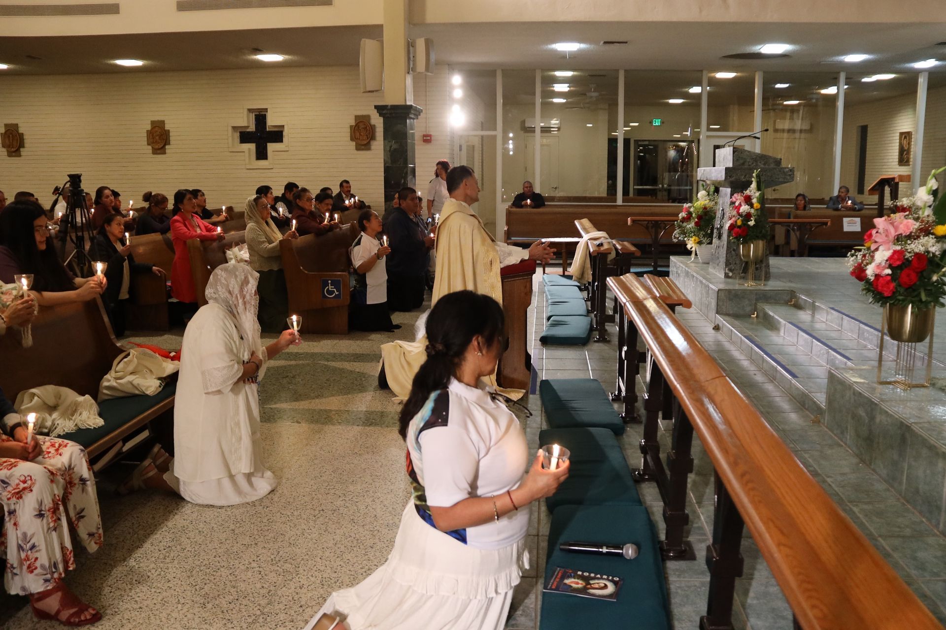 People kneeling in prayer inside a church, facing an altar with flowers and candles.