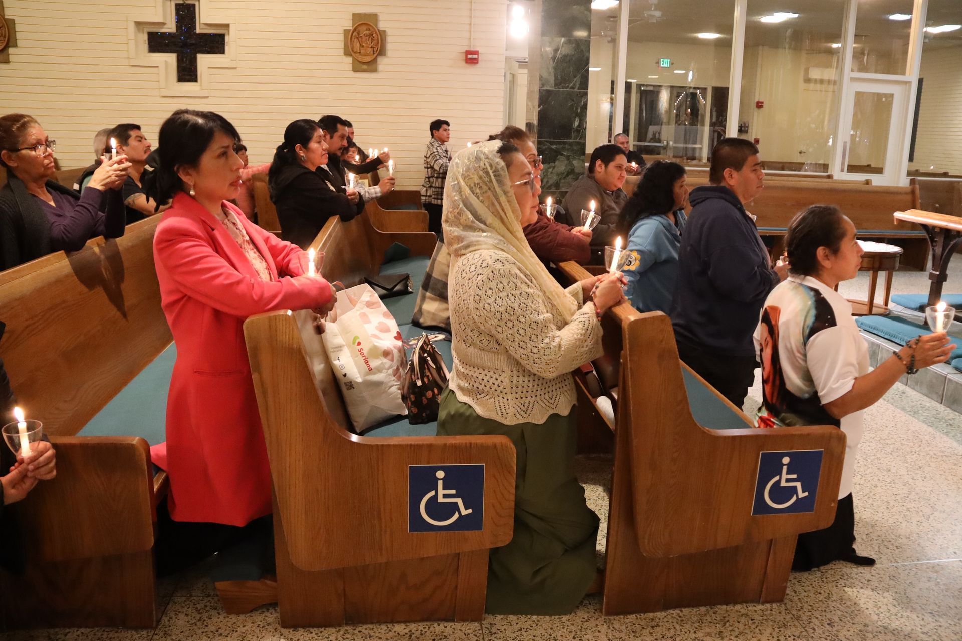 People seated in church pews during a service, with wheelchair-accessible seating signs visible.