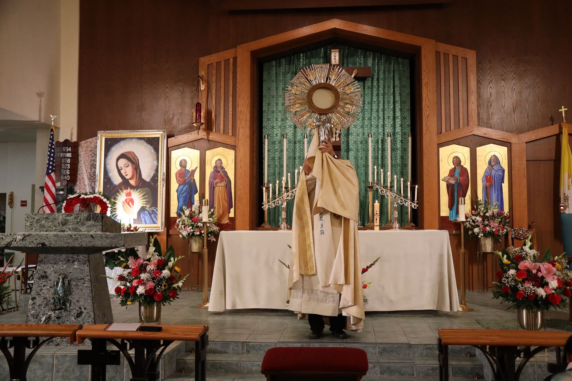 Church altar with a priest in white vestments before a gold monstrance and religious icons