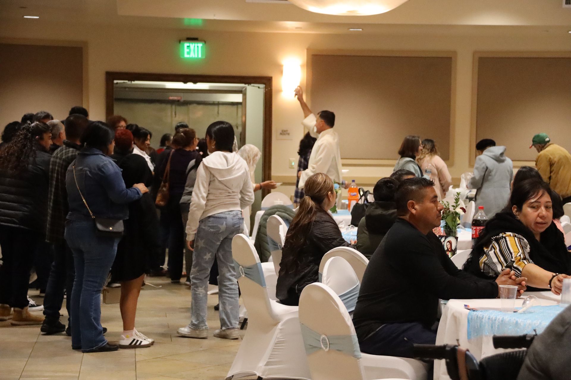 People mingling at a banquet hall reception with tables, chairs, and warm wall lighting