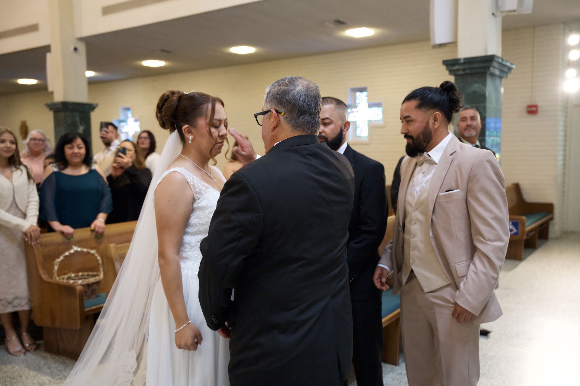 Bride and groom stand with officiant in a church aisle during the wedding ceremony