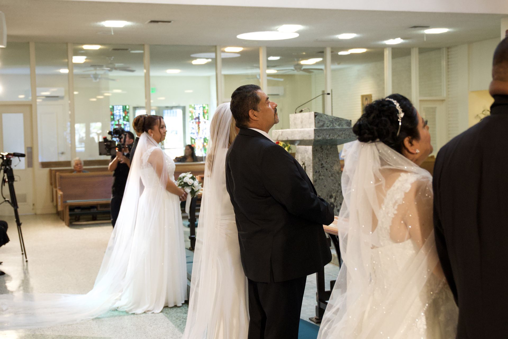 People in formal attire stand in line inside a bright indoor event hall, facing forward.