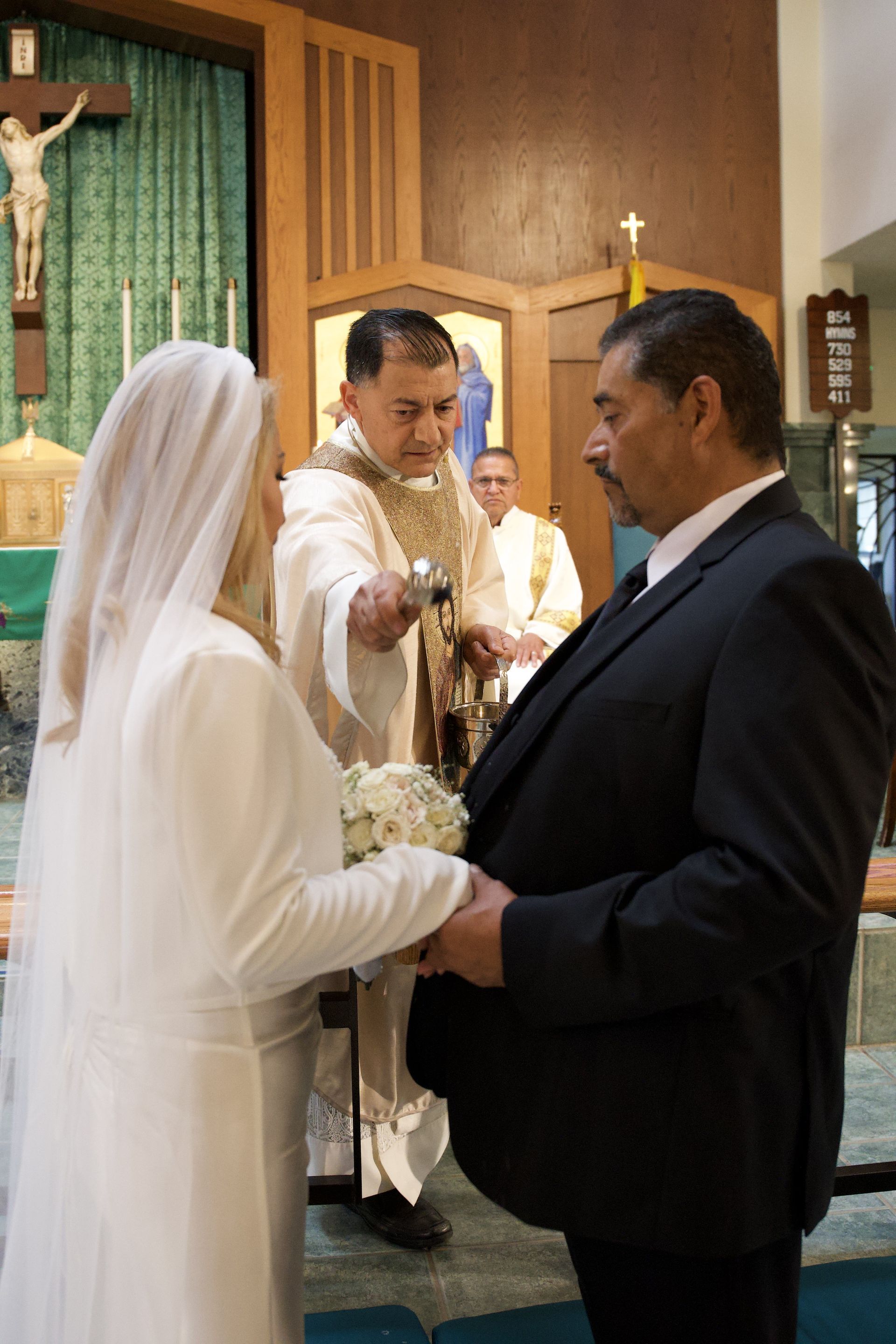 Bride and groom holding hands during a wedding ceremony before a priest in a church