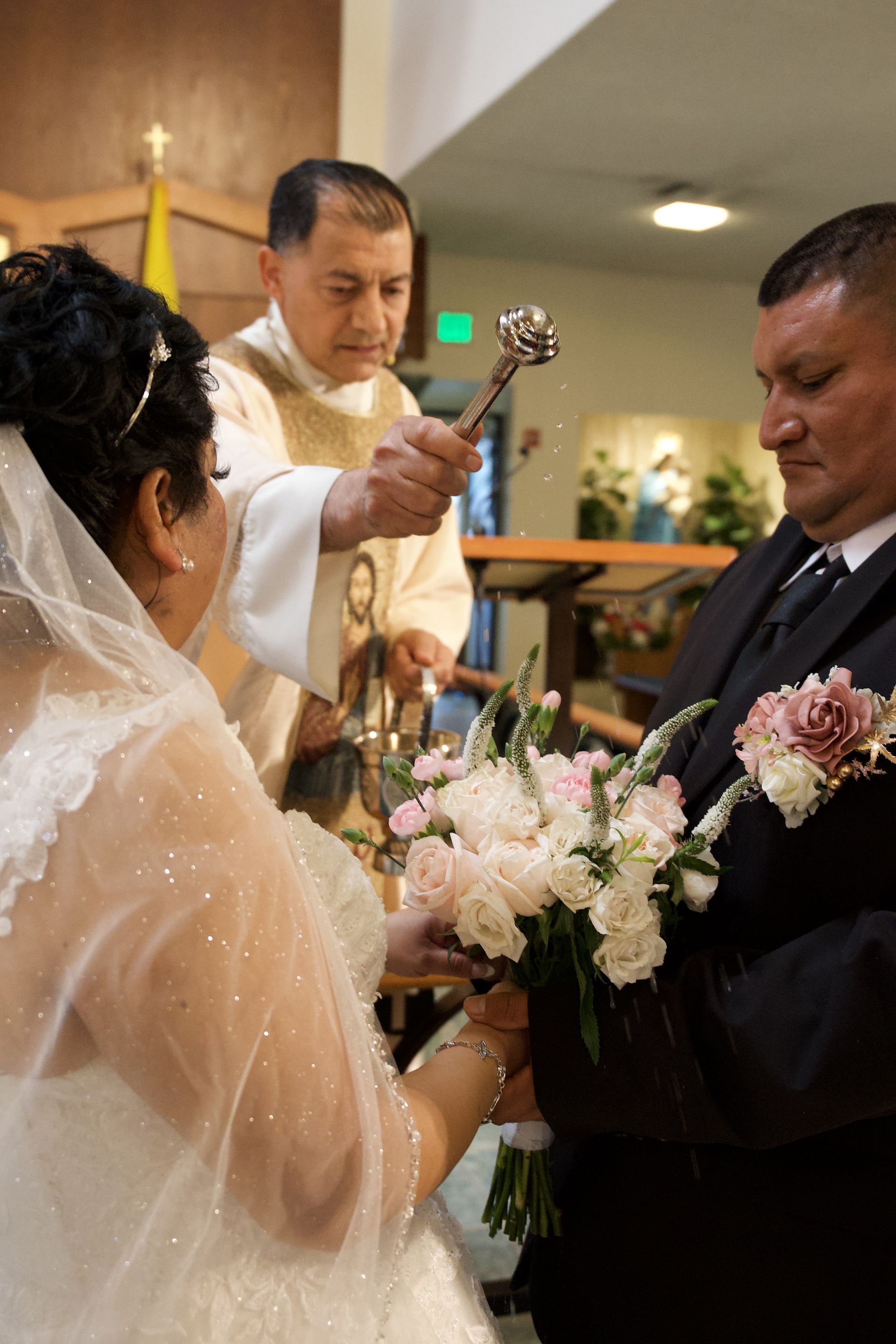 Wedding officiant blesses a couple during a church ceremony as they exchange flowers and vows