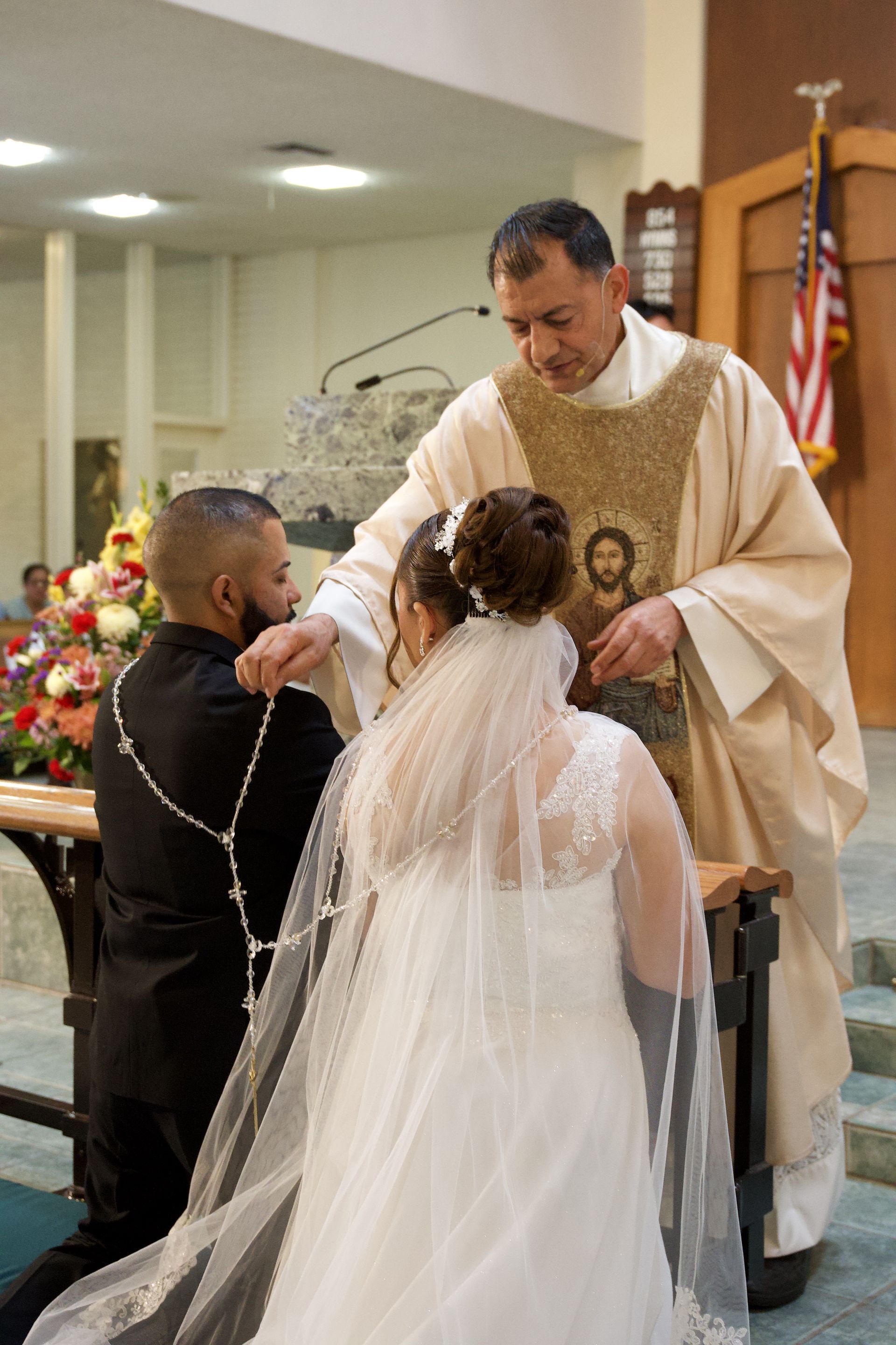 Bride and groom kneel before a priest during a church wedding ceremony