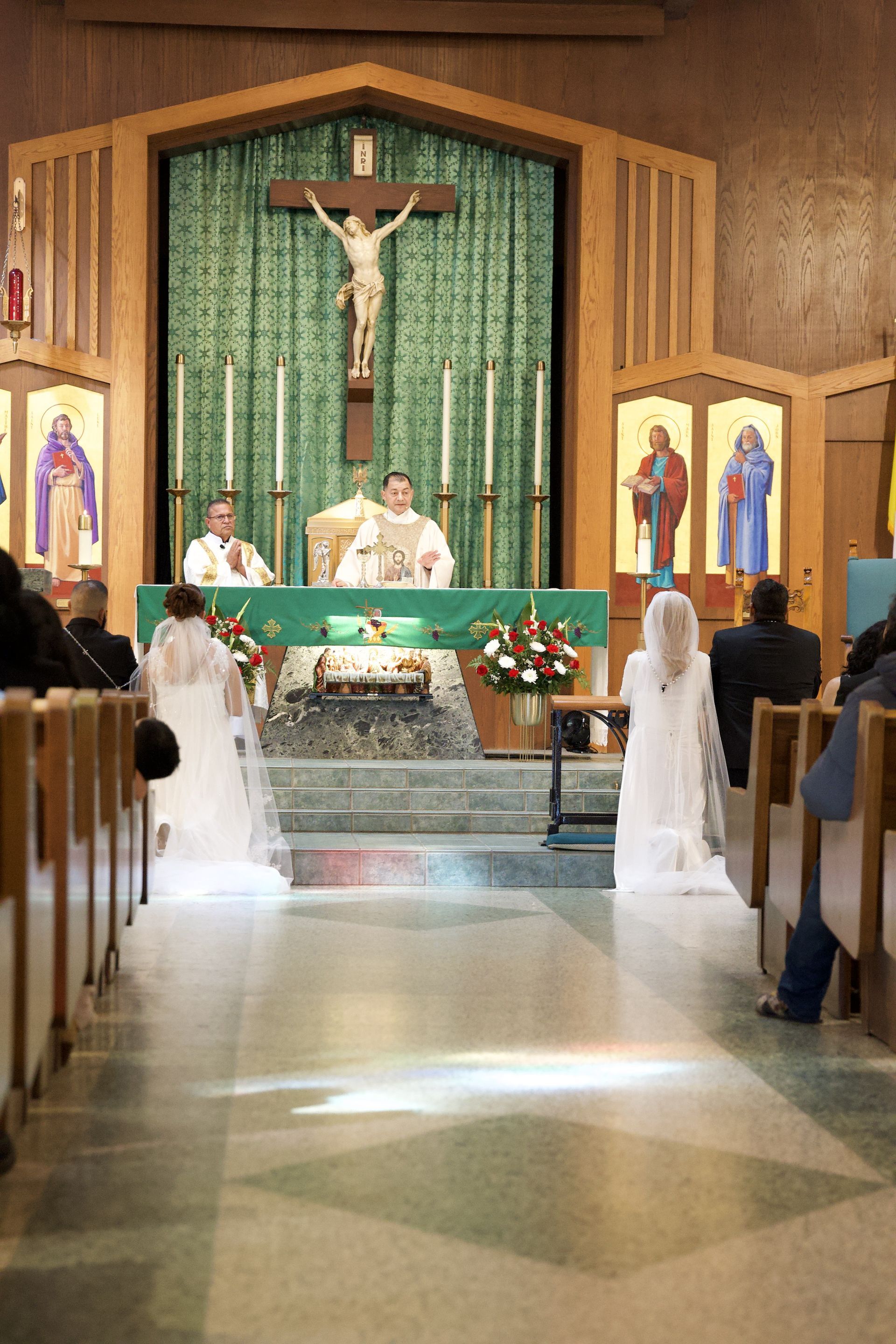 Church wedding ceremony at altar with bride and groom, priest, crucifix, and guests seated in pews